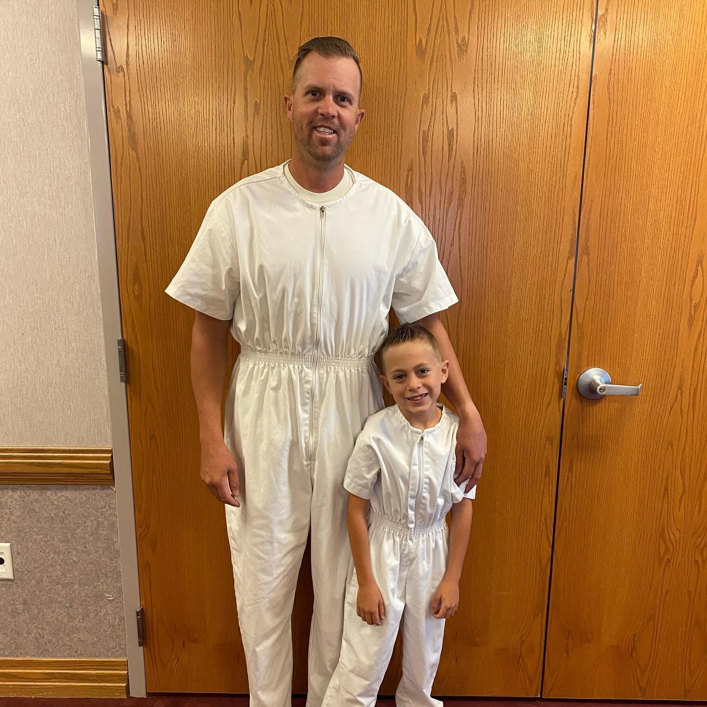 Fire Captain Spencer Long wraps his arm around one of his young sons, both wearing matching, full-body white zippered outfits. This proud father-son moment shows the quiet and guiding influence Spencer had in his family's lives. | Source: Facebook/katrina.g.long