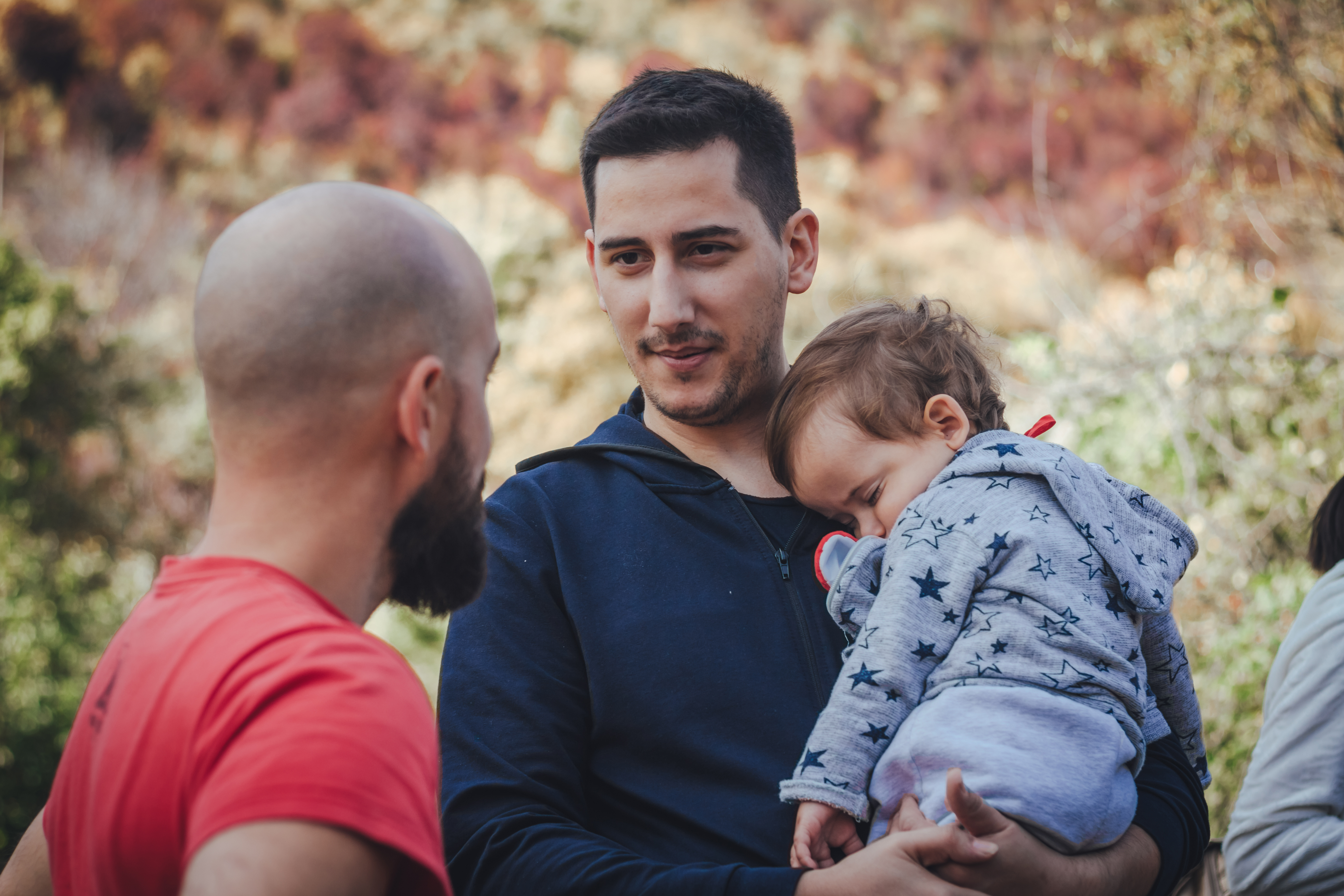 Two men talking and one of them holding a baby | Source: Shutterstock