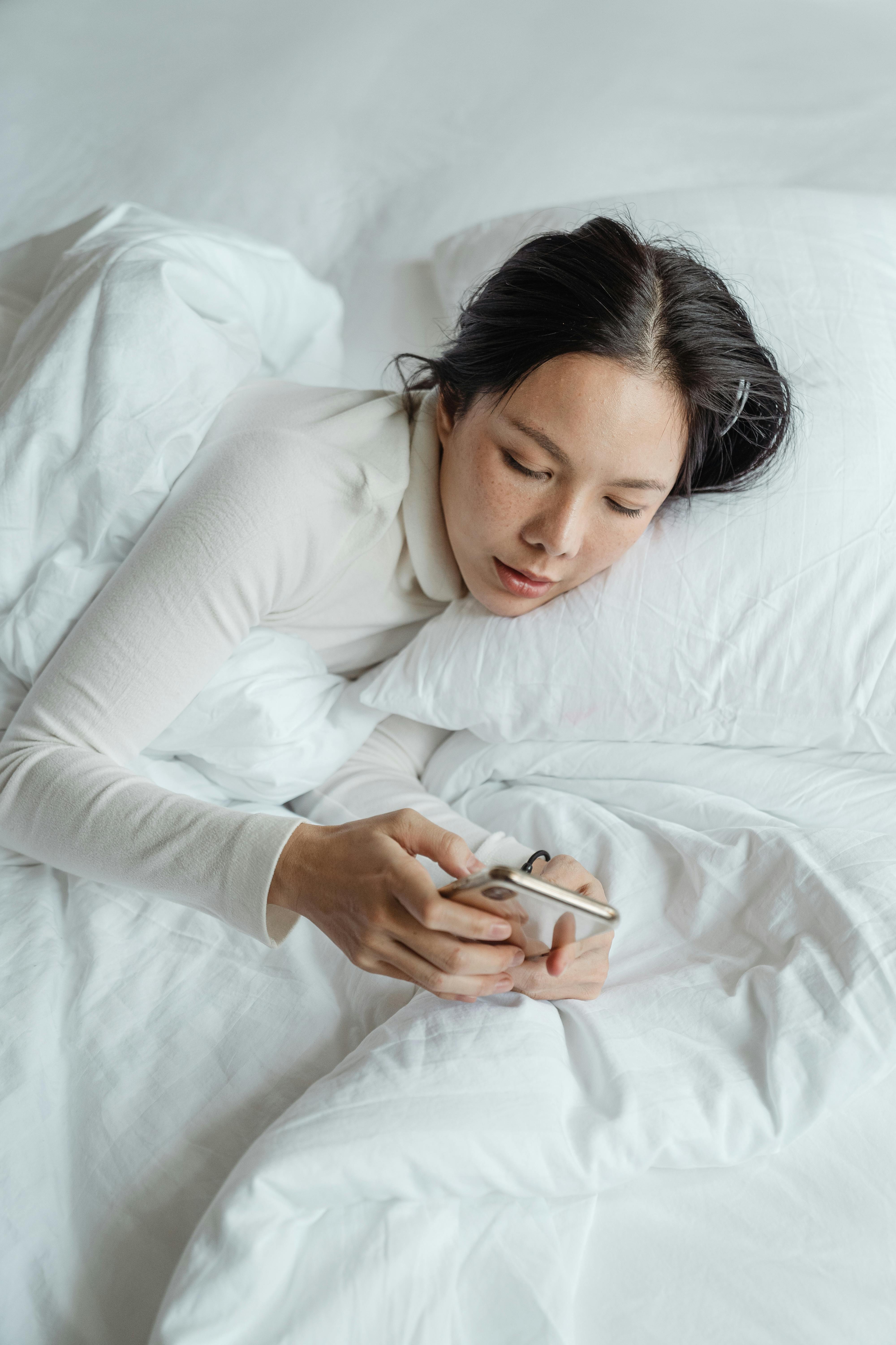 A woman texting on her phone while lying in bed | Source: Pexels