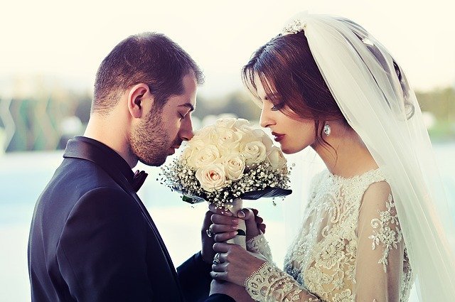 Bride and groom sniff a bouquet of flowers | Photo: Pixabay