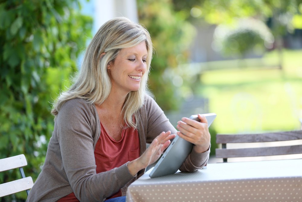 Mujer de cabello largo y rubio usando su tableta en un parque. | Foto: Shutterstock
