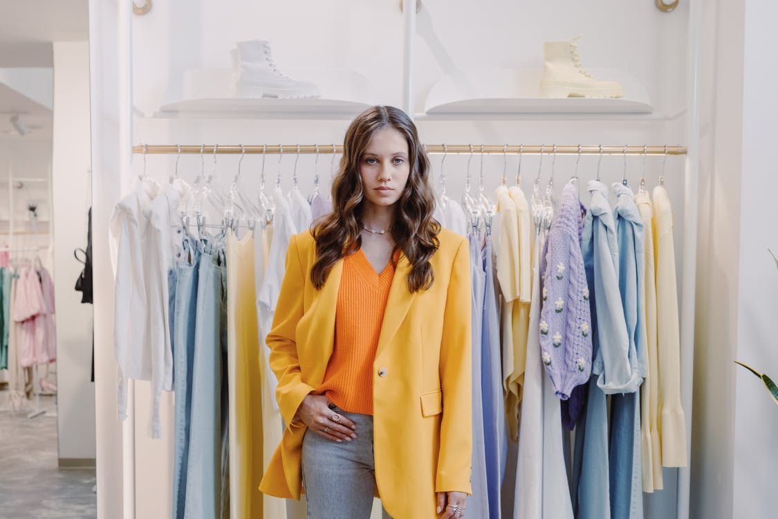 Una mujer parada frente a unas prendas de vestir colgadas en una tienda. | Foto: Pexels