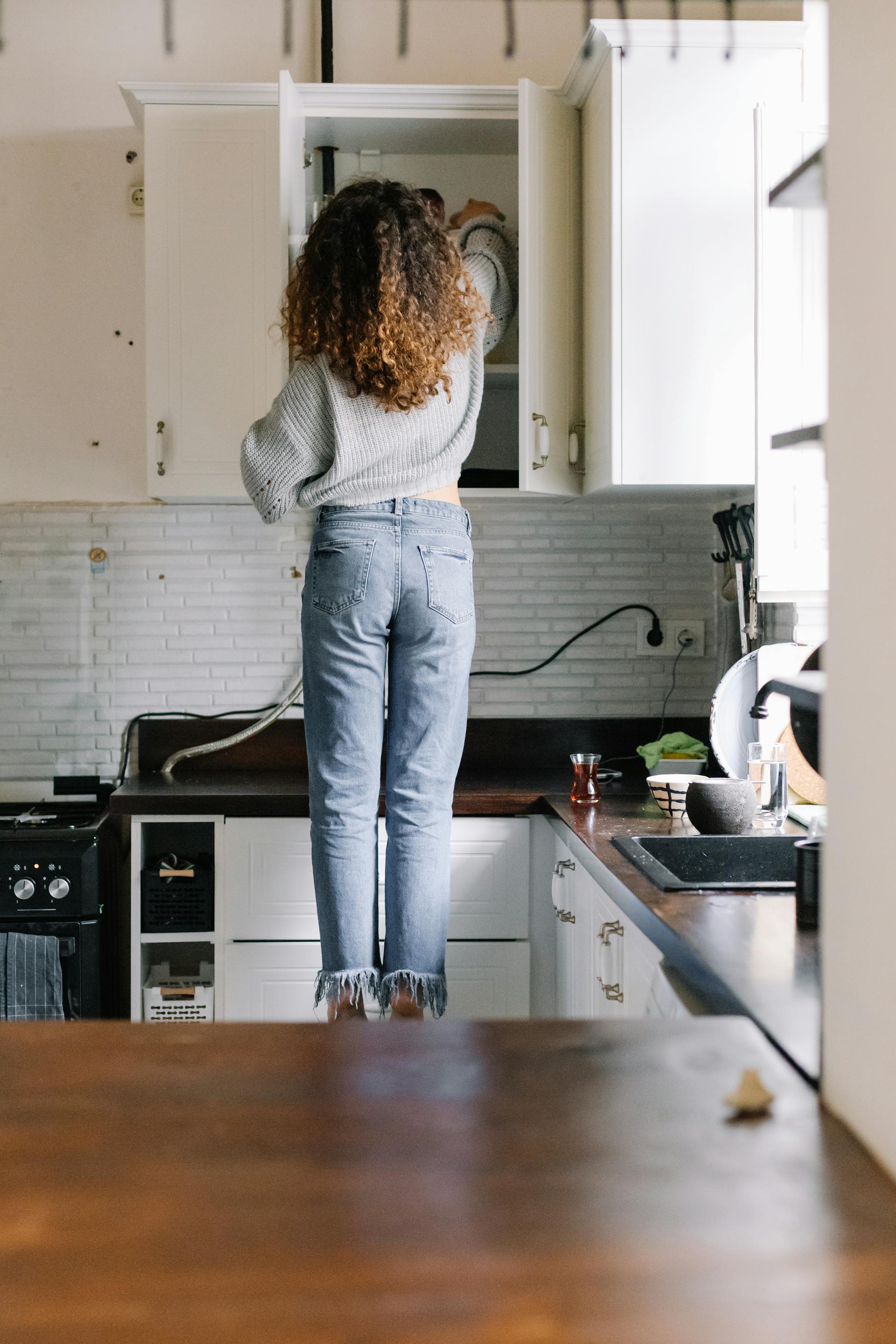 Rear view of a woman opening a kitchen cabinet | Source: Pexels