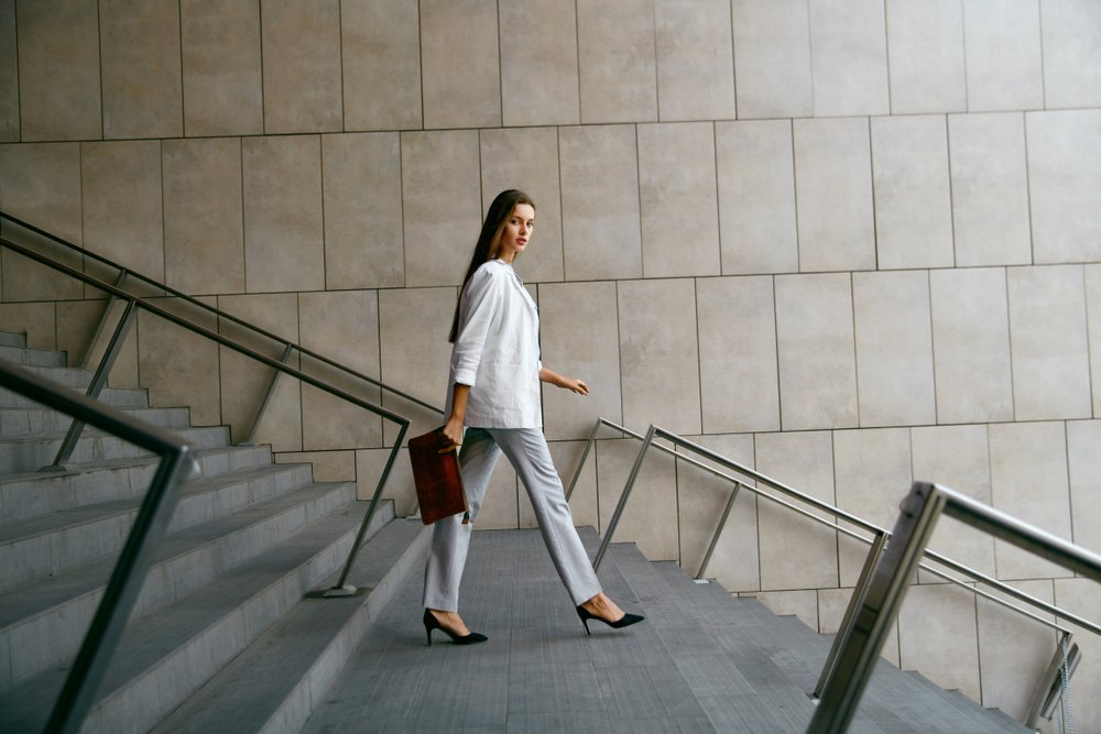 Mujer sonriente en ropa de oficina elegante bajando las escaleras. | Fuente: Shutterstock