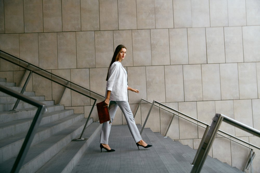Mujer sonriente en ropa de oficina elegante bajando las escaleras. | Fuente: Shutterstock Mujer sonriente en ropa de oficina elegante bajando las escaleras. | Fuente: Shutterstock