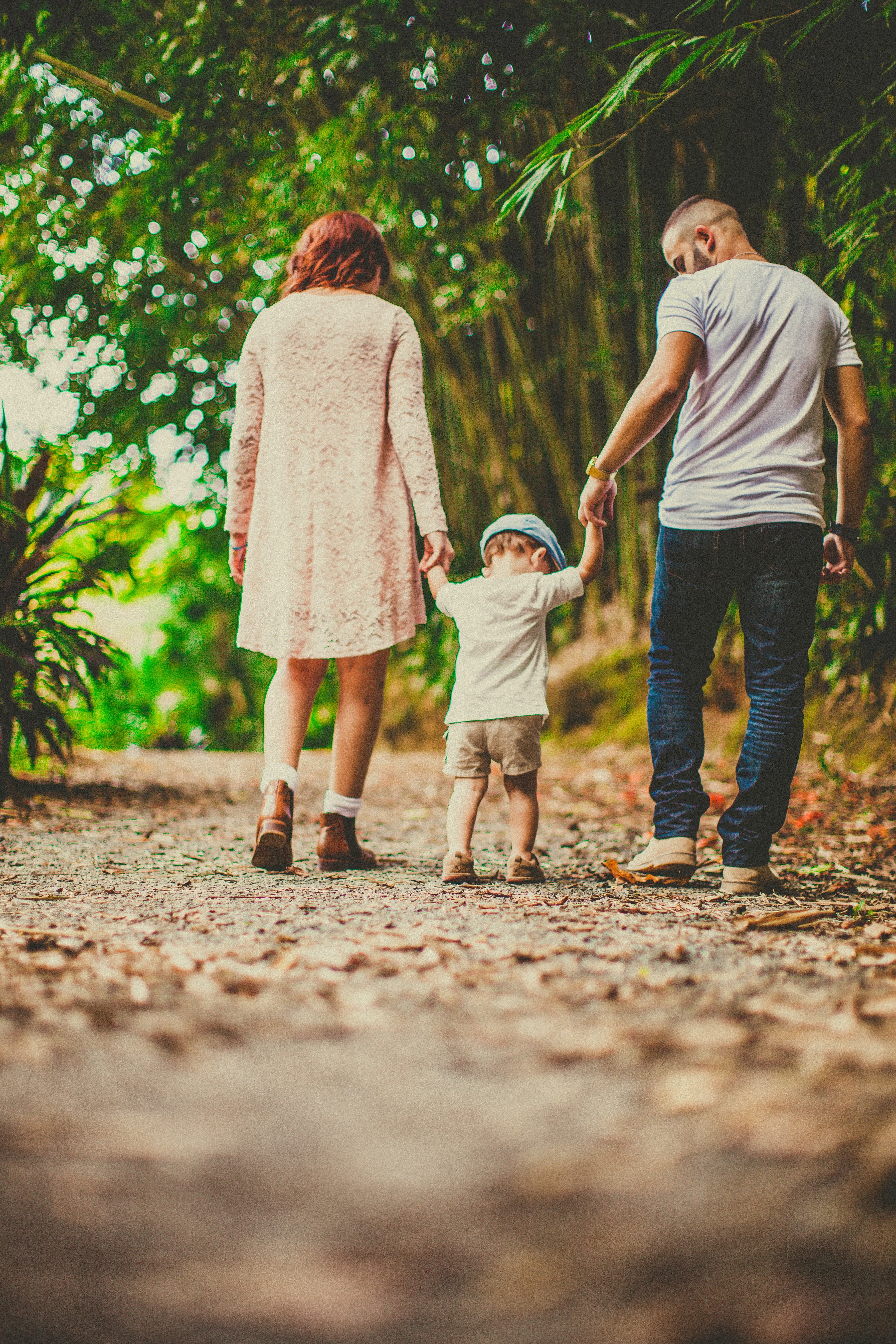 A couple with their son holding his hands on each side walking in an unpaved pathway outdoors | Source: Pexels 