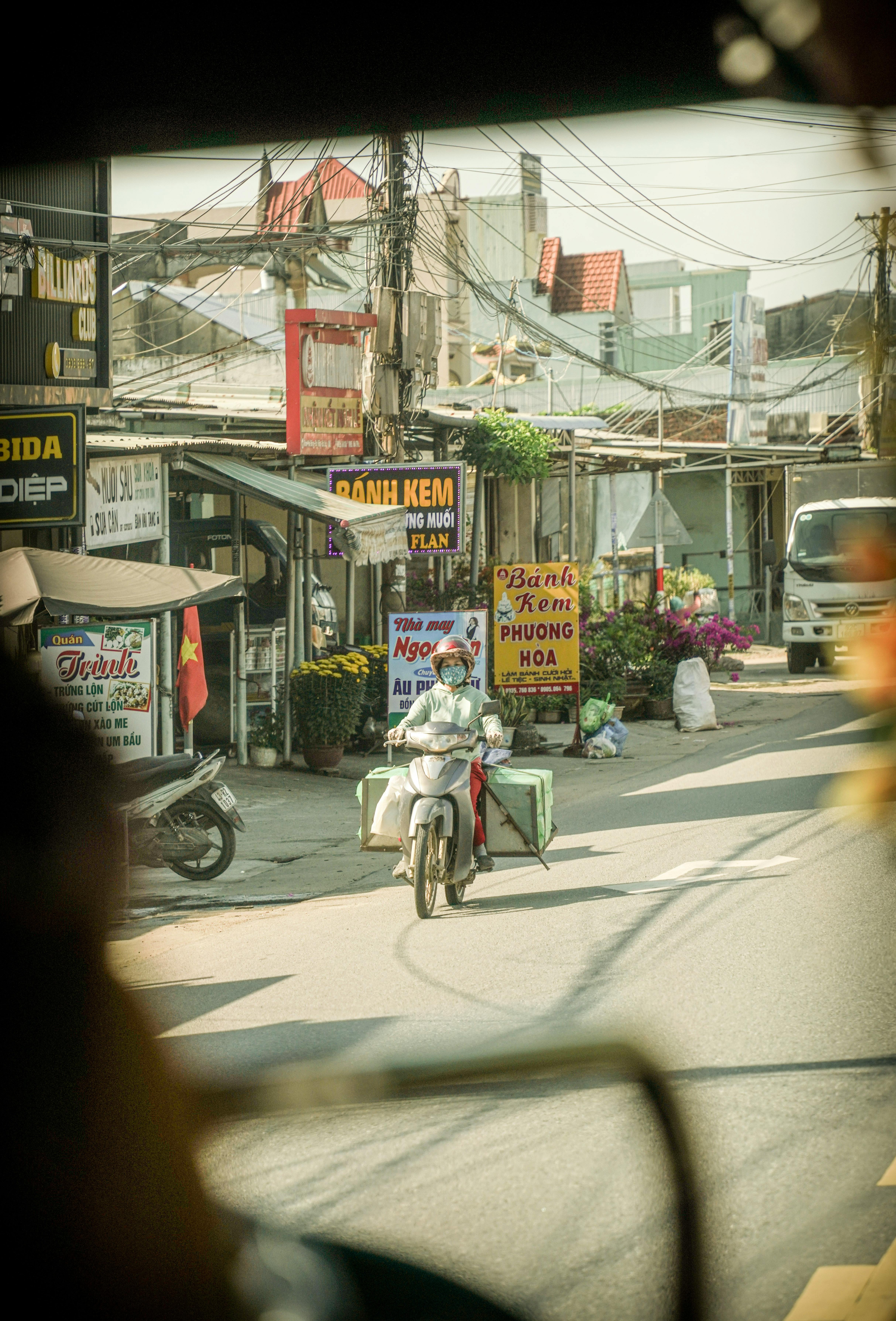A motorcyclist travels along a roadside lined with small businesses and tangled overhead wires in Vietnam | Source: Pexels