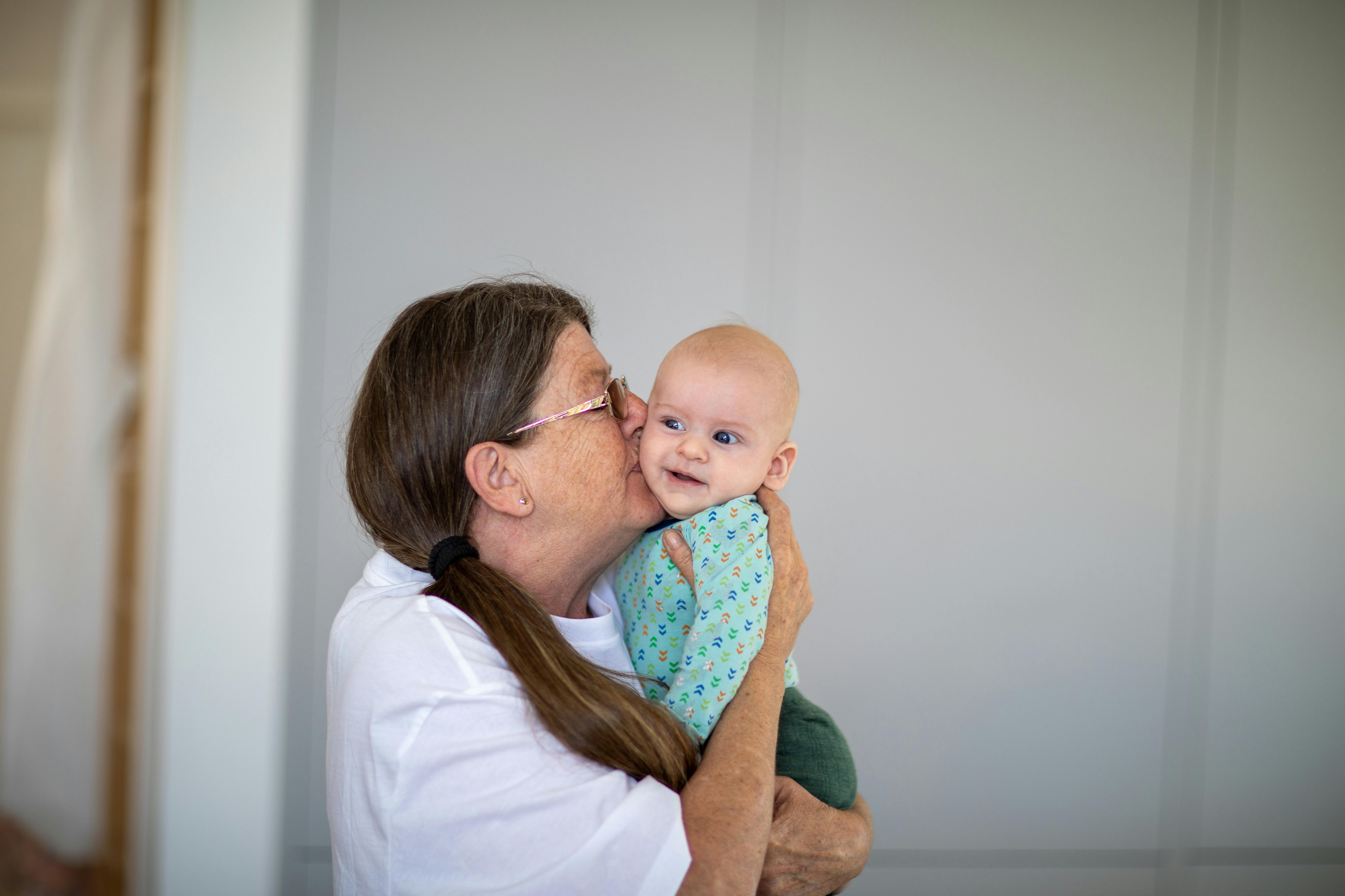 A senior woman kissing a baby on the cheek | Source: Pexels