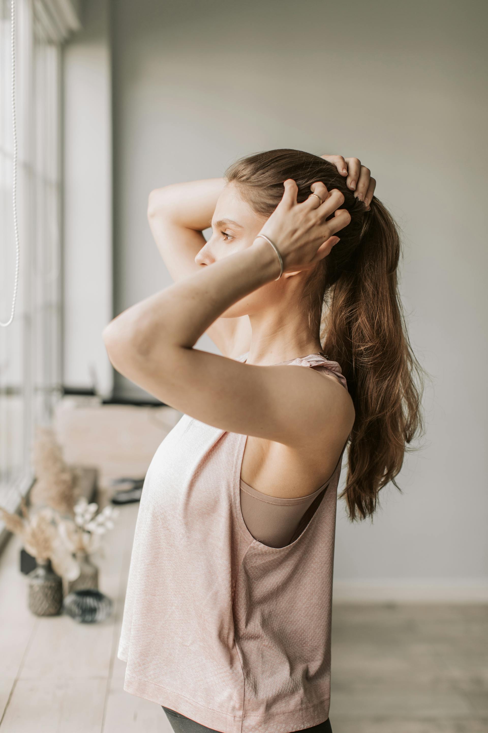 A woman tying her hair while standing near the window | Source: Pexels