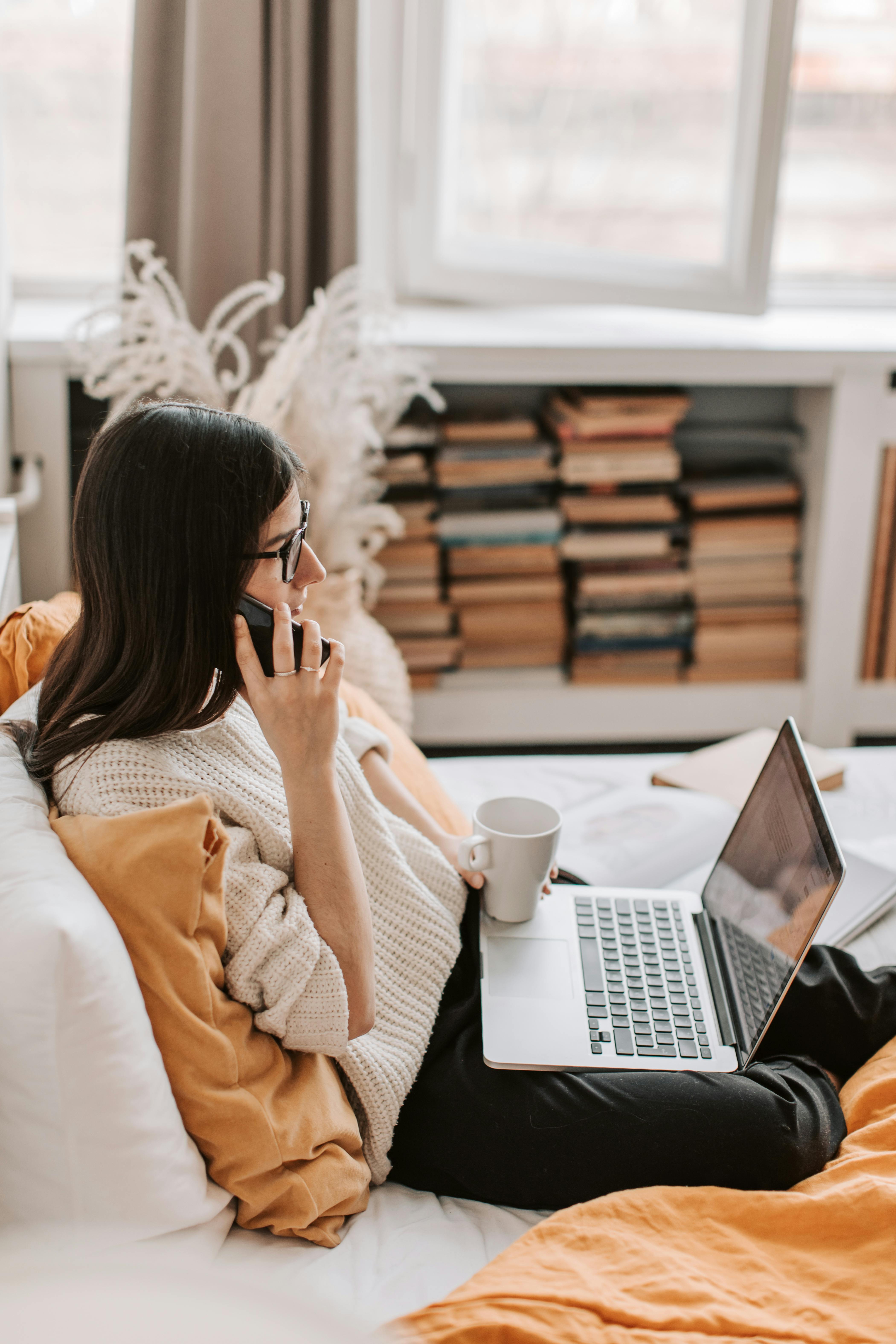 A woman on a phone call at home, with her laptop in front of her | Source: Pexels