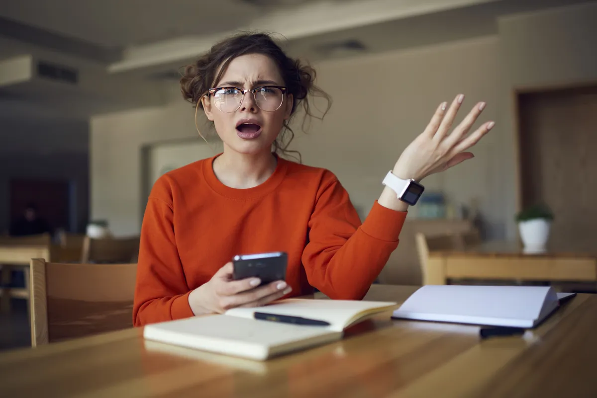 Eine Frau sieht wütend und überrascht aus über das, was sie auf ihrem Handy sieht. | Source: Shutterstock