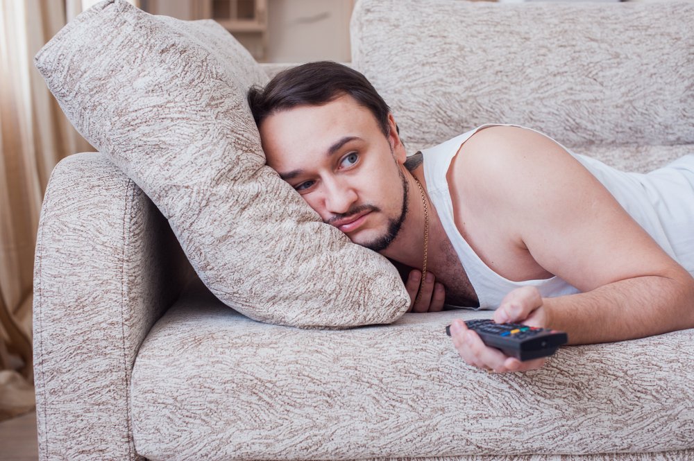 Un homme face contre terre sur un canapé changeant de chaîne de télévision. | Source : Shutterstock Un homme face contre terre sur un canapé changeant de chaîne de télévision. | Source : Shutterstock