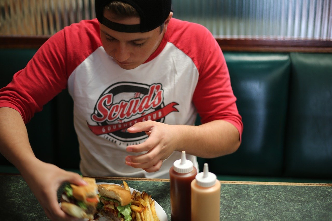 A photo of a man eating a burger. | Photo: Pixabay