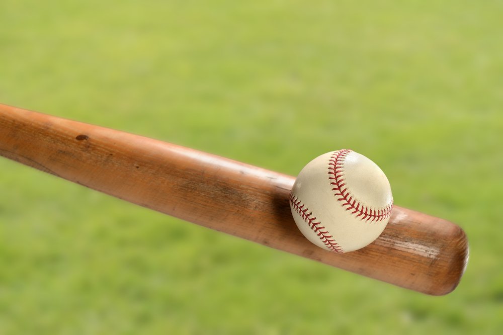 Baseball bat hitting ball over grass | Photo: Shutterstock