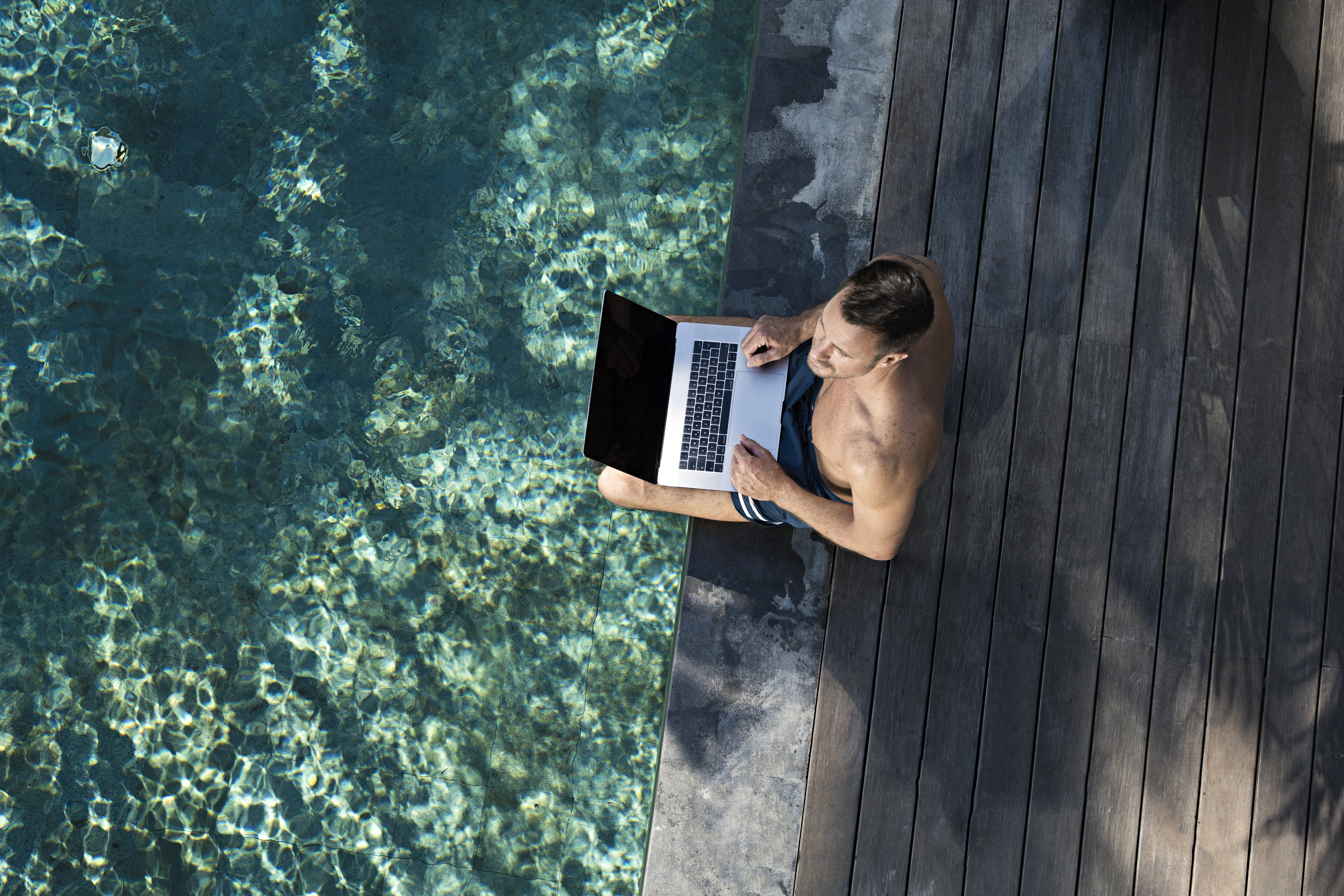 Mature man sitting at the poolside, using laptop | Source: Getty Images