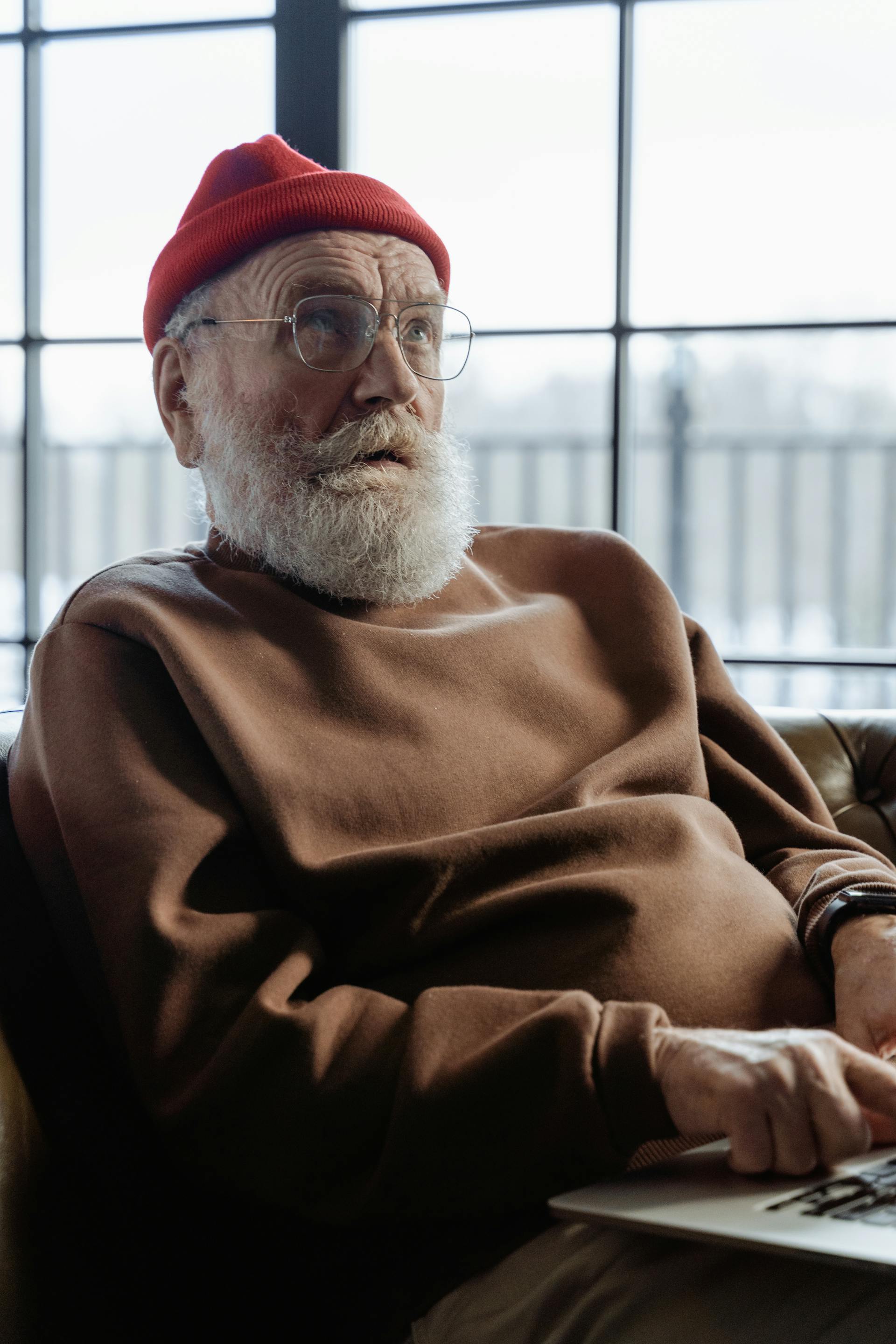 A senior man in red beanie sitting in a chair and looking at someone | Source: Pexels