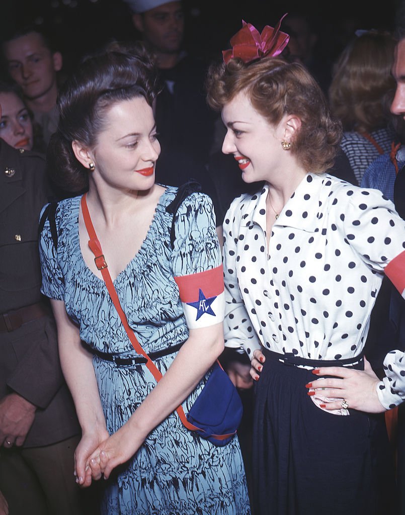 Joan Fontaine and Olivia de Havilland smile at each other as they attend an event at the Hollywood Canteen, Los Angeles, California on January 1,1940. | Photo: Getty Images.