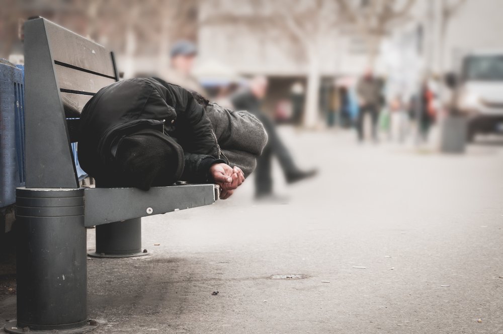 Persona sin hogar acostada en la banqueta de una plaza. | Foto: Shutterstock