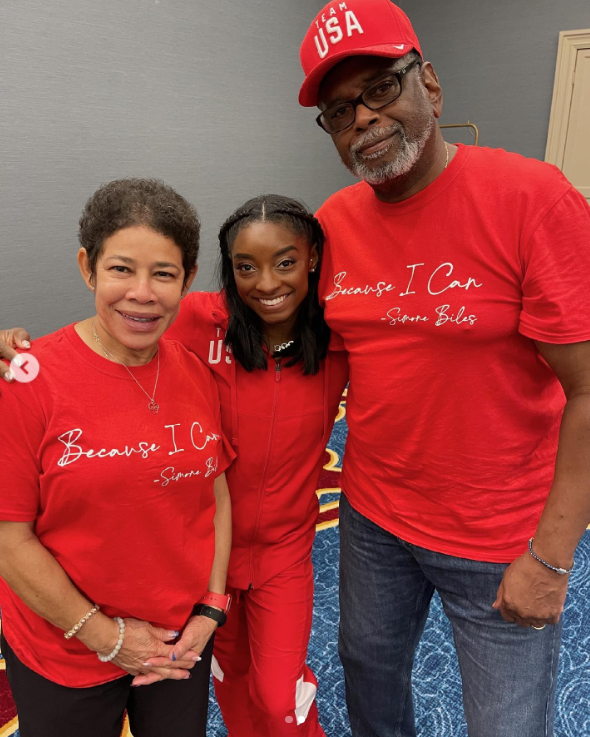 Simone Biles, in a red sweater and pants, smiles between her parents, Nellie and Ronald Biles, who are wearing matching red shirts, posted in June 2021 | Source: Instagram.com/simonebiles