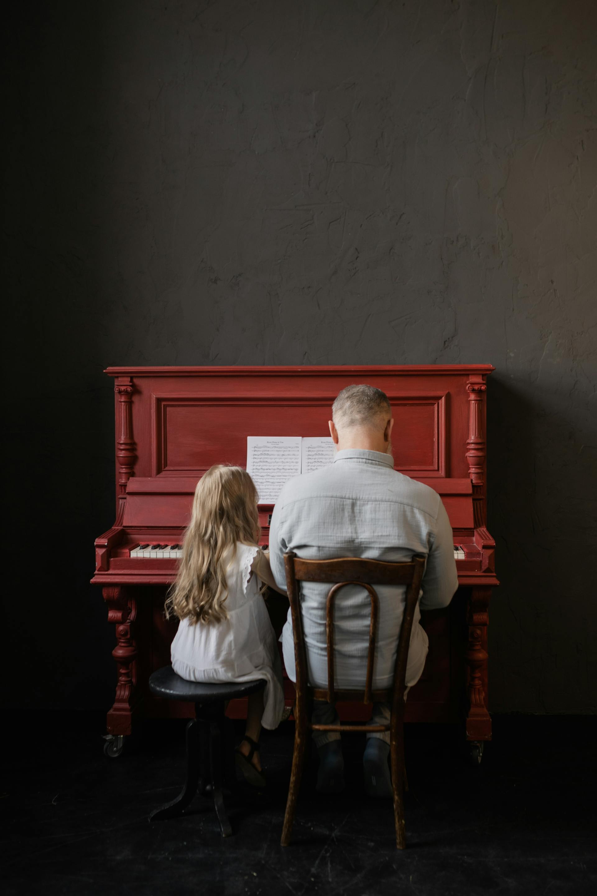 Back view shot of a grandfather-granddaughter duo playing a piano | Source: Pexels