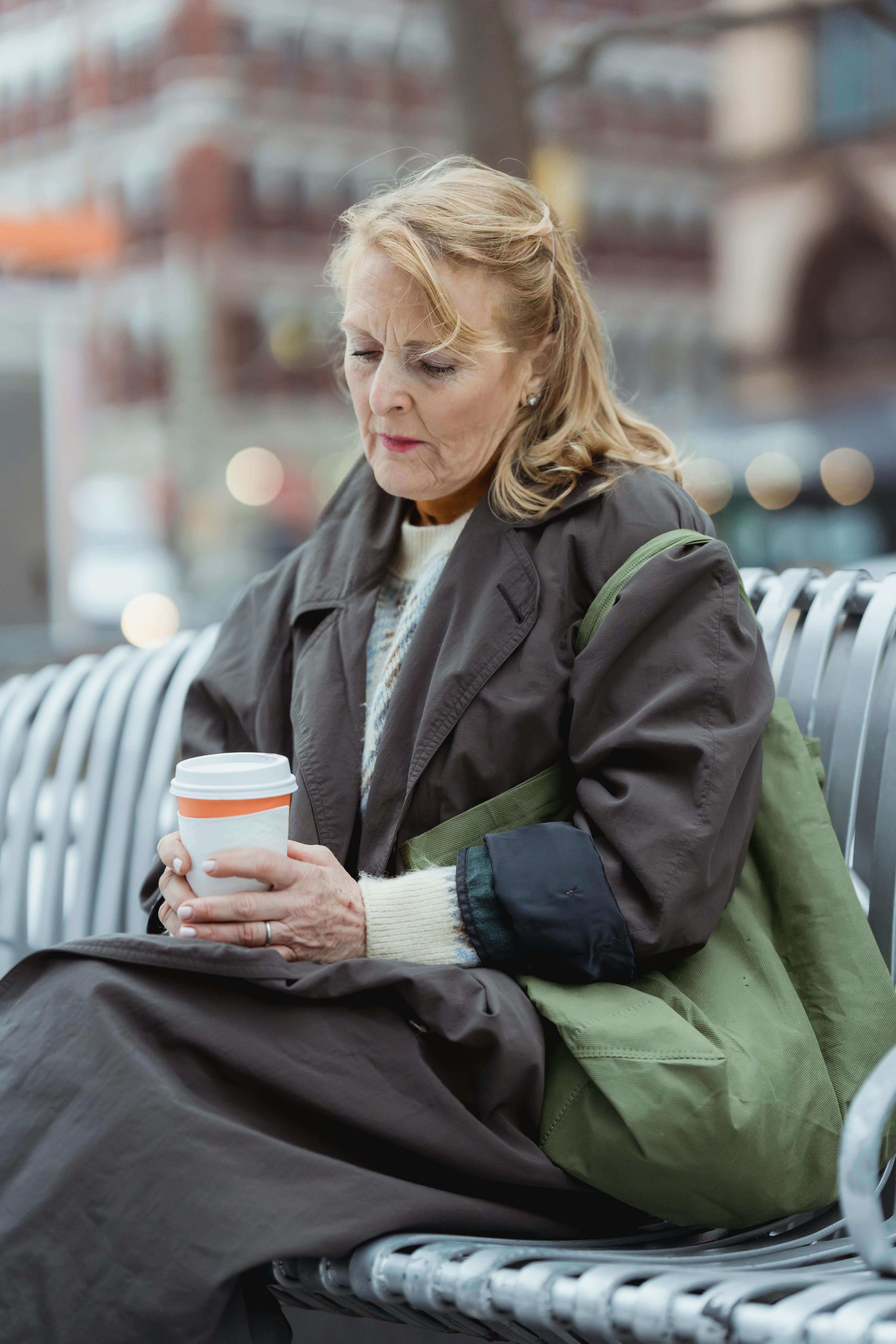 An upset older woman sitting on a bench holding a beverage | Source: Pexels