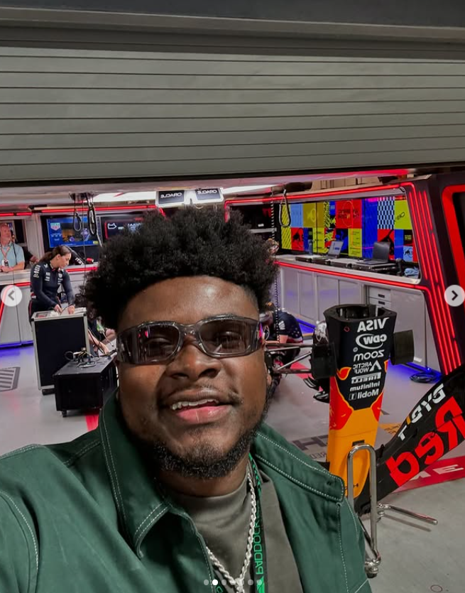 Marquay Collins smiles in front of a Formula 1 pit garage, as posted in December 2024 | Source: Instagram/marquaythegoat