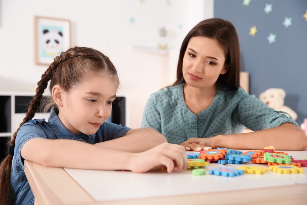 Mujer joven y niña con trastorno autista jugando en casa . | Fuente: Shutterstock