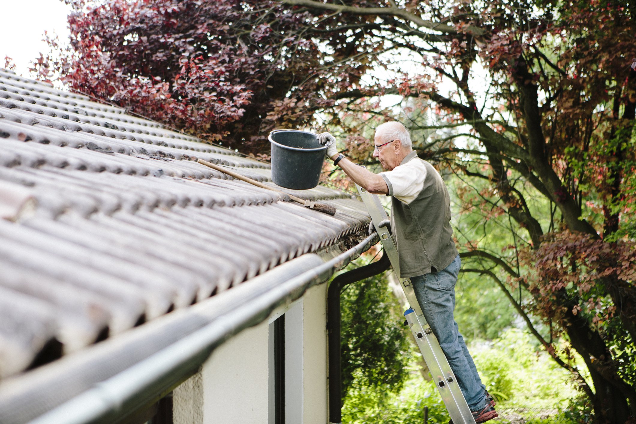 Ein älterer Mann steht auf Leiter und reinigt eine Dachrinne | Quelle: Getty Images