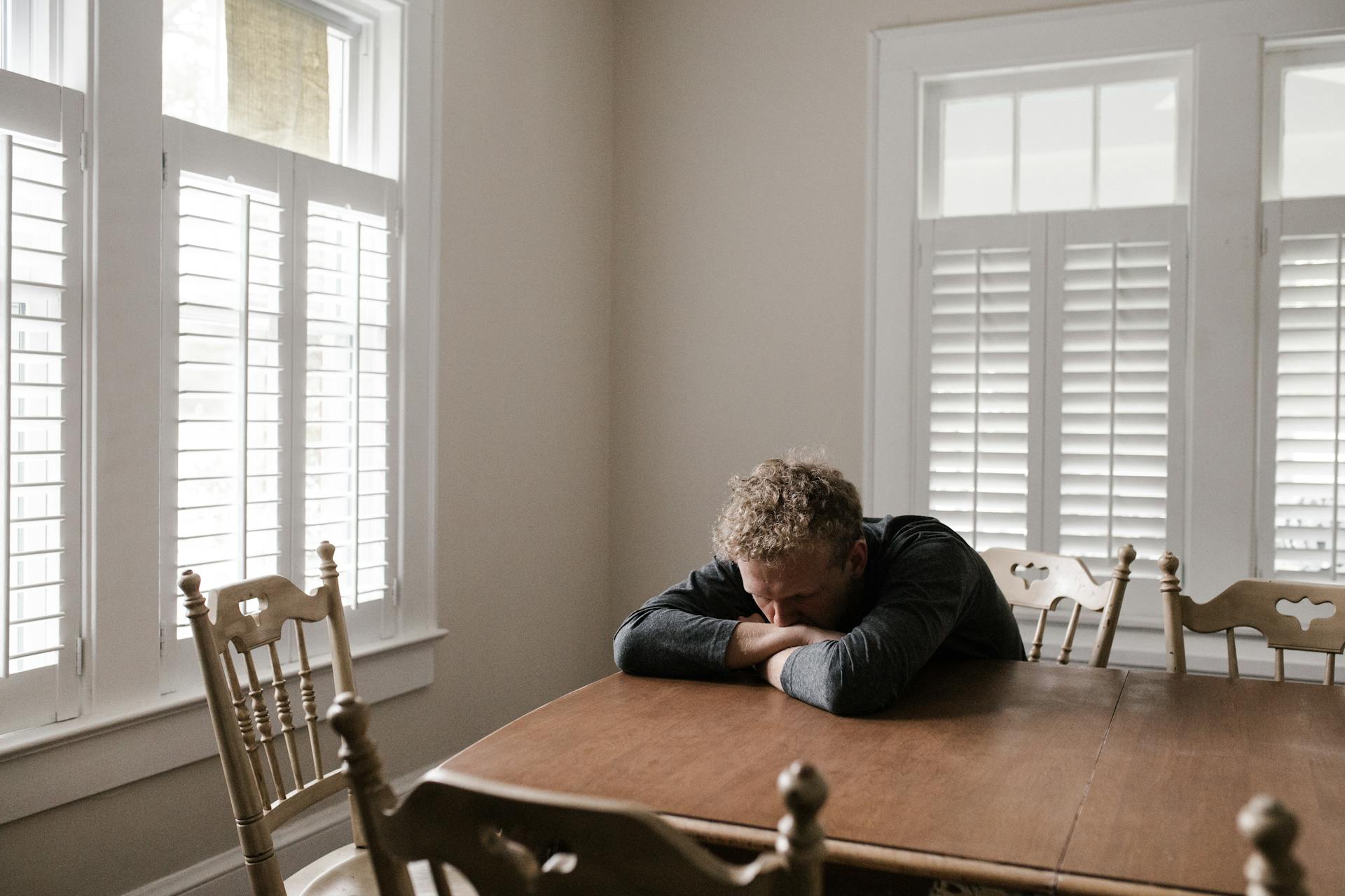 Man resting his head on his arms at his kitchen table | Source: Pexels