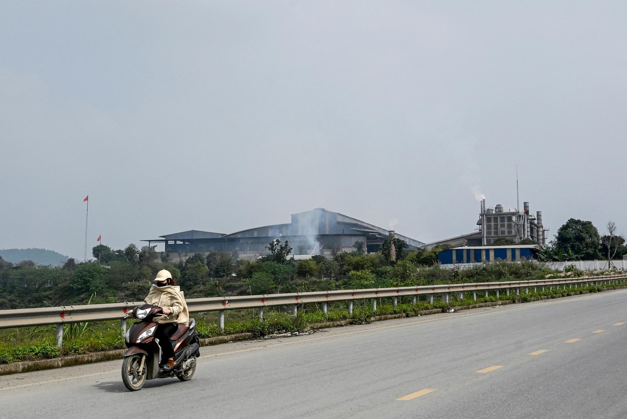 A woman photographed riding a motorbike past the Duc Giang Lao Cai chemical plant in the Tang Loong Industrial Park on 19 March 2026 in Lao Cai Province, northern Vietnam. | Source: Getty Images