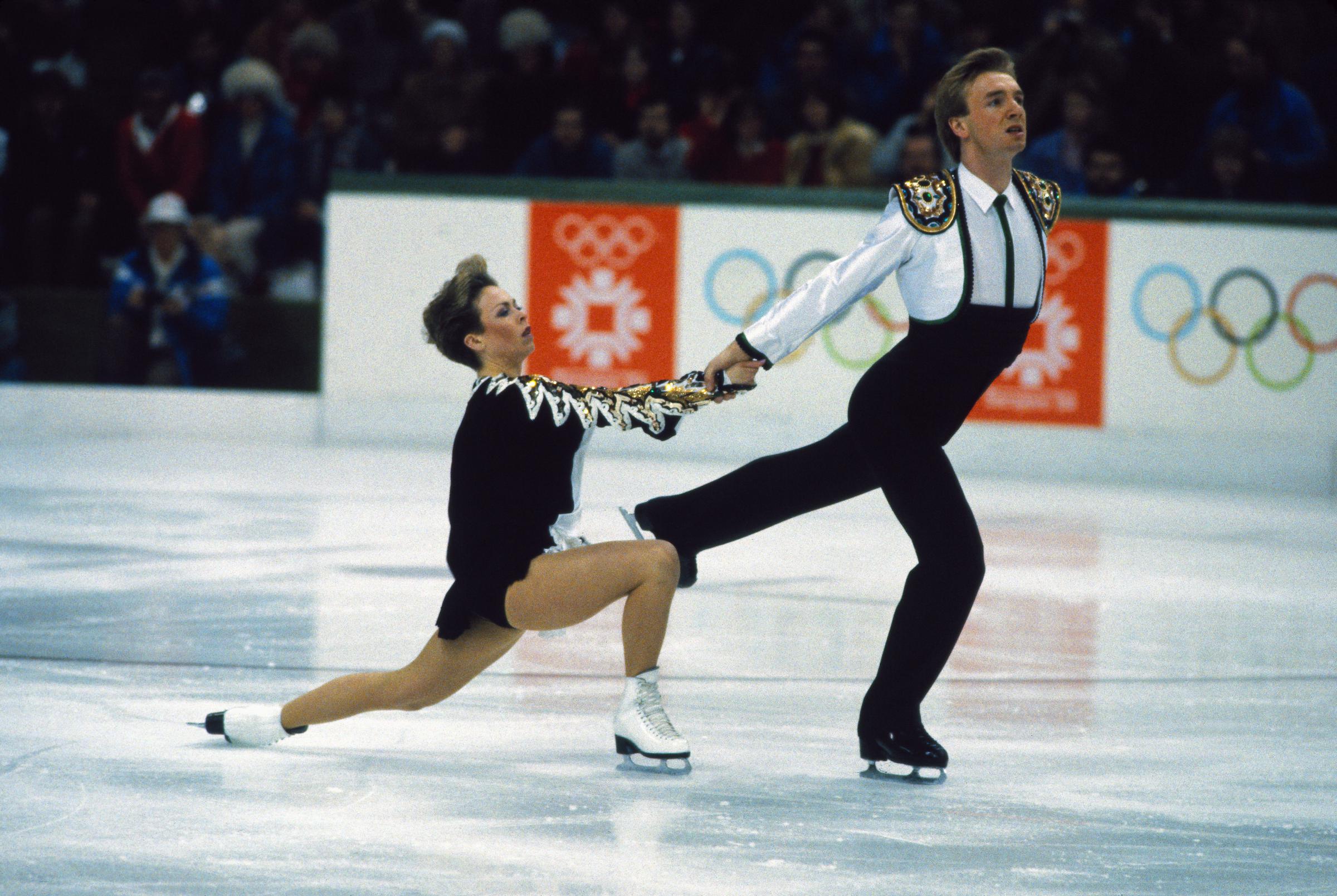 Torvill and Dean perform a powerful sequence during their 1984 Winter Olympics routine in Sarajevo. Dean drives forward with a strong extended leg as Torvill sinks into a deep lunge, their clasped hands anchoring the movement.