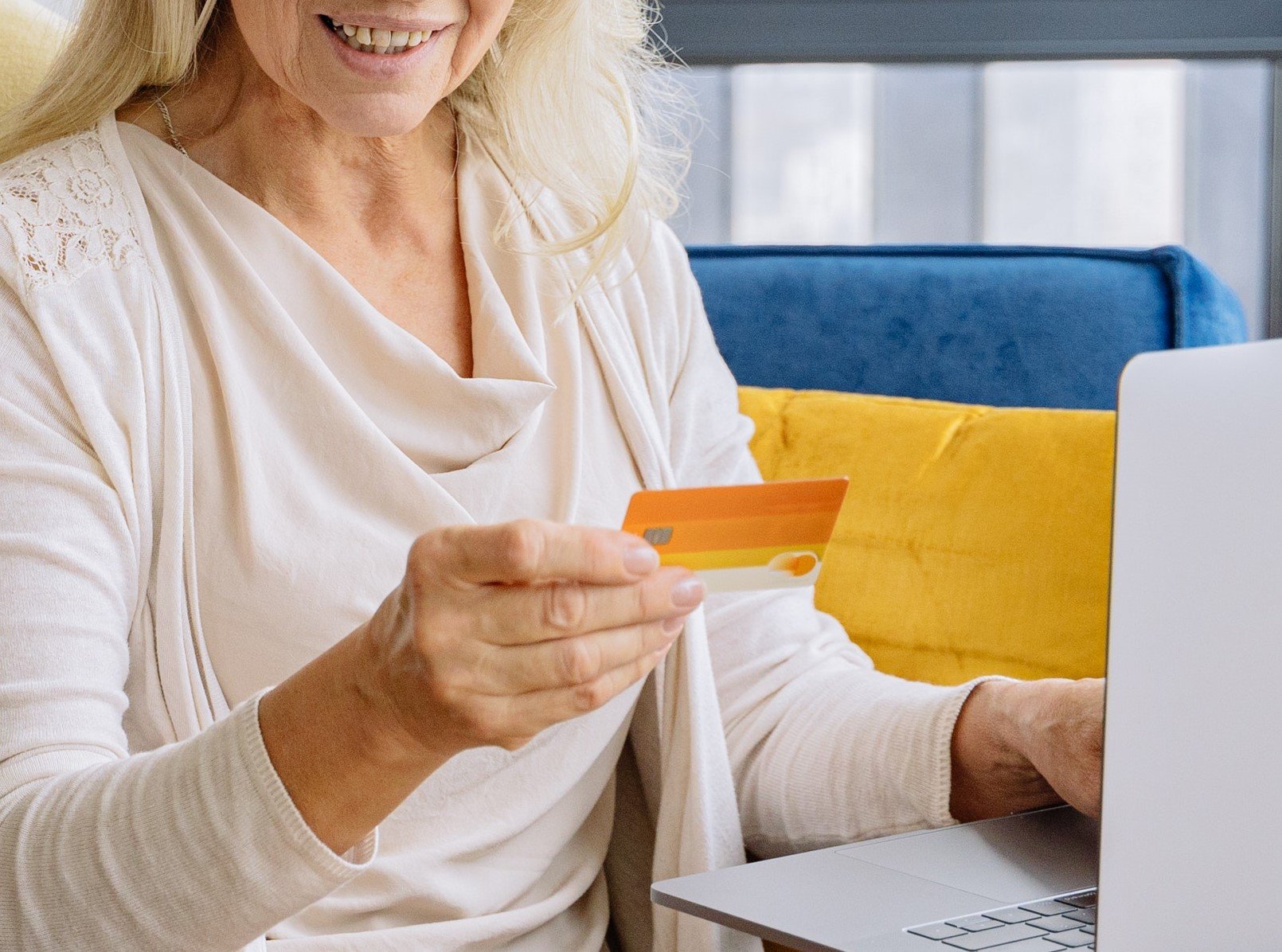 Una mujer mayor sentada frente a una computadora portátil mientras sostiene una tarjeta. | Foto: Pexels