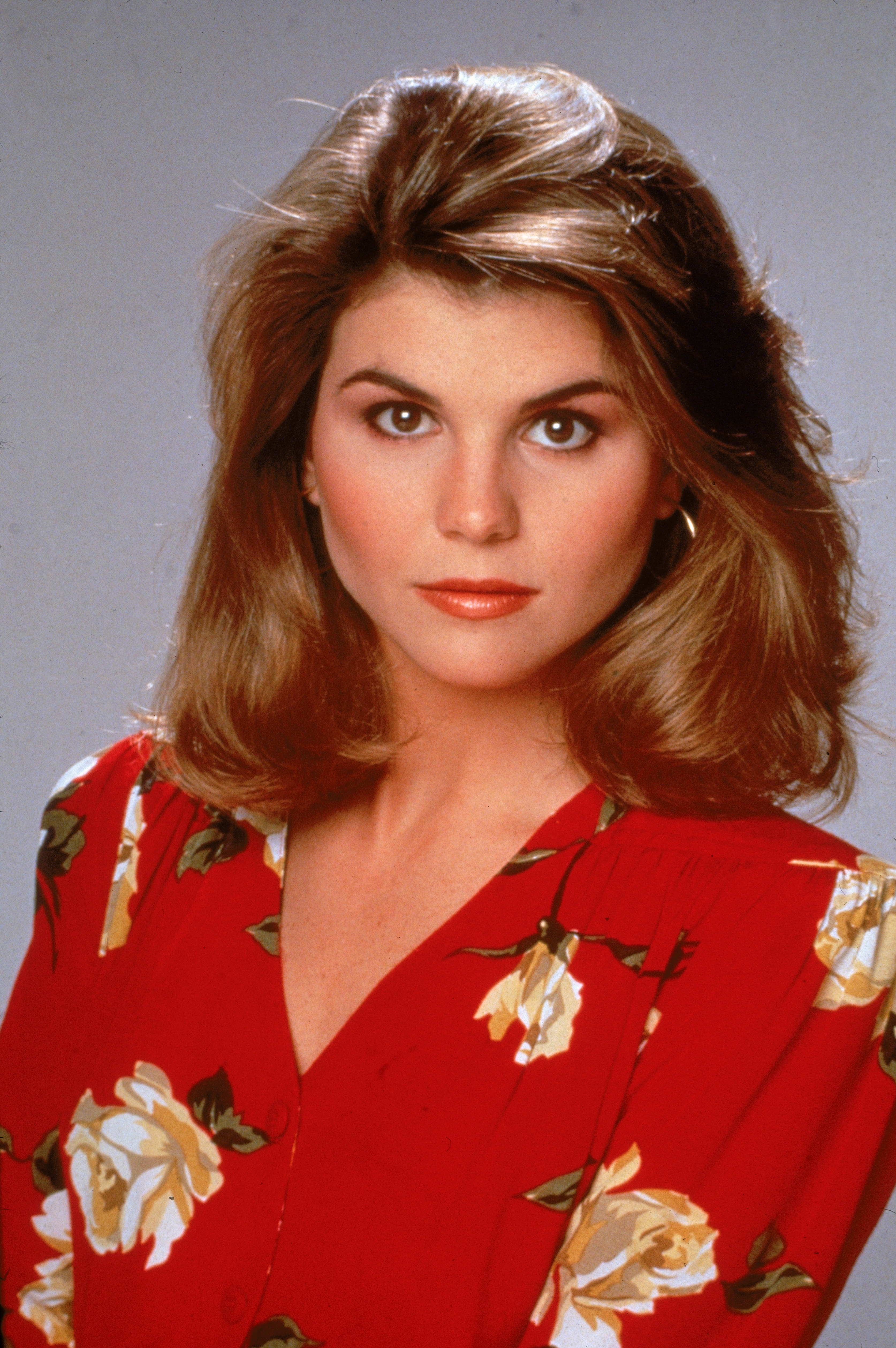 Lori Loughlin was captured in a studio portrait for the television series "Full House," circa 1989, wearing a red floral blouse with softly styled hair framing her face.