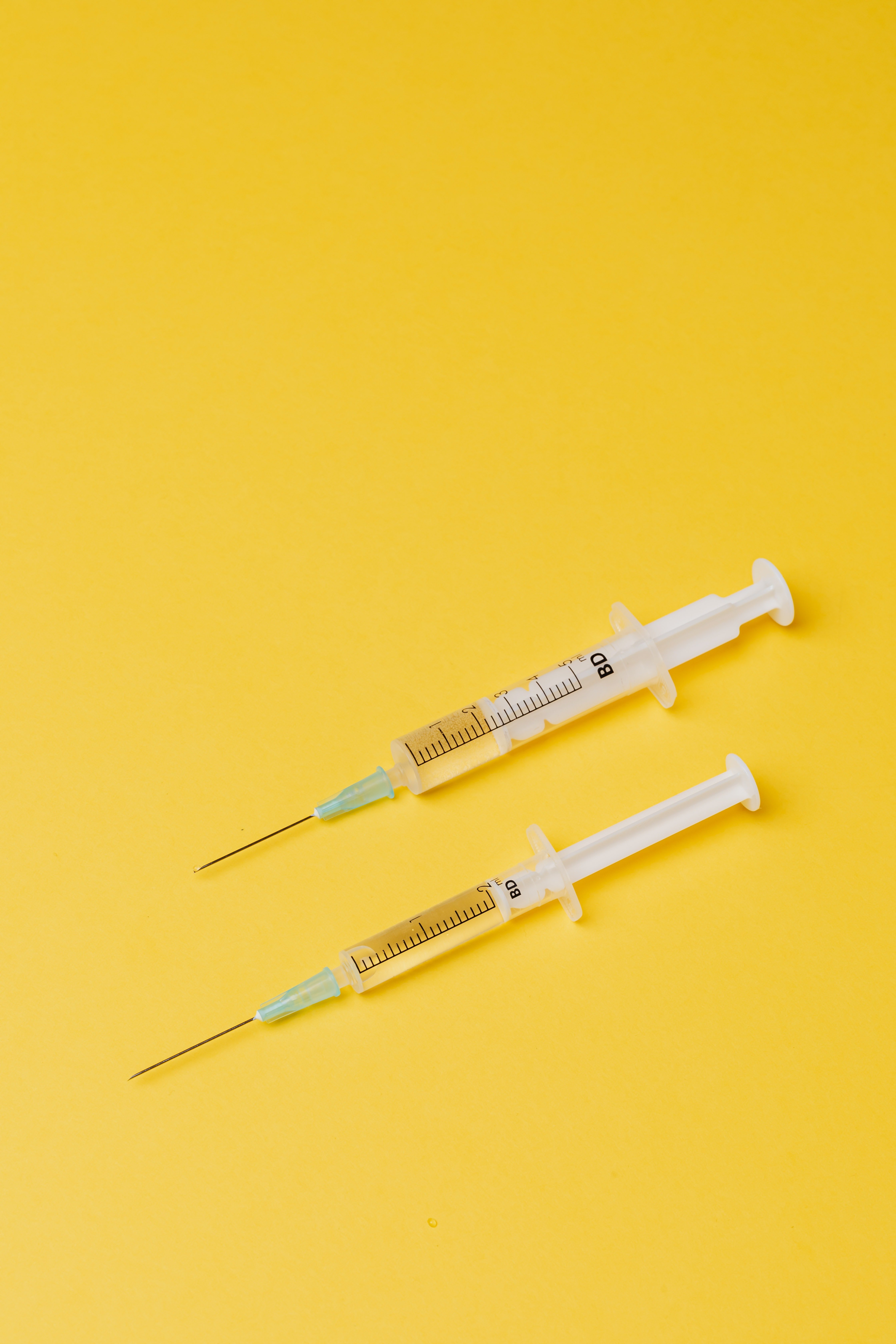 Photo of two injections against a yellow backdrop. | Source: Pexels/ Karolina Grabowska