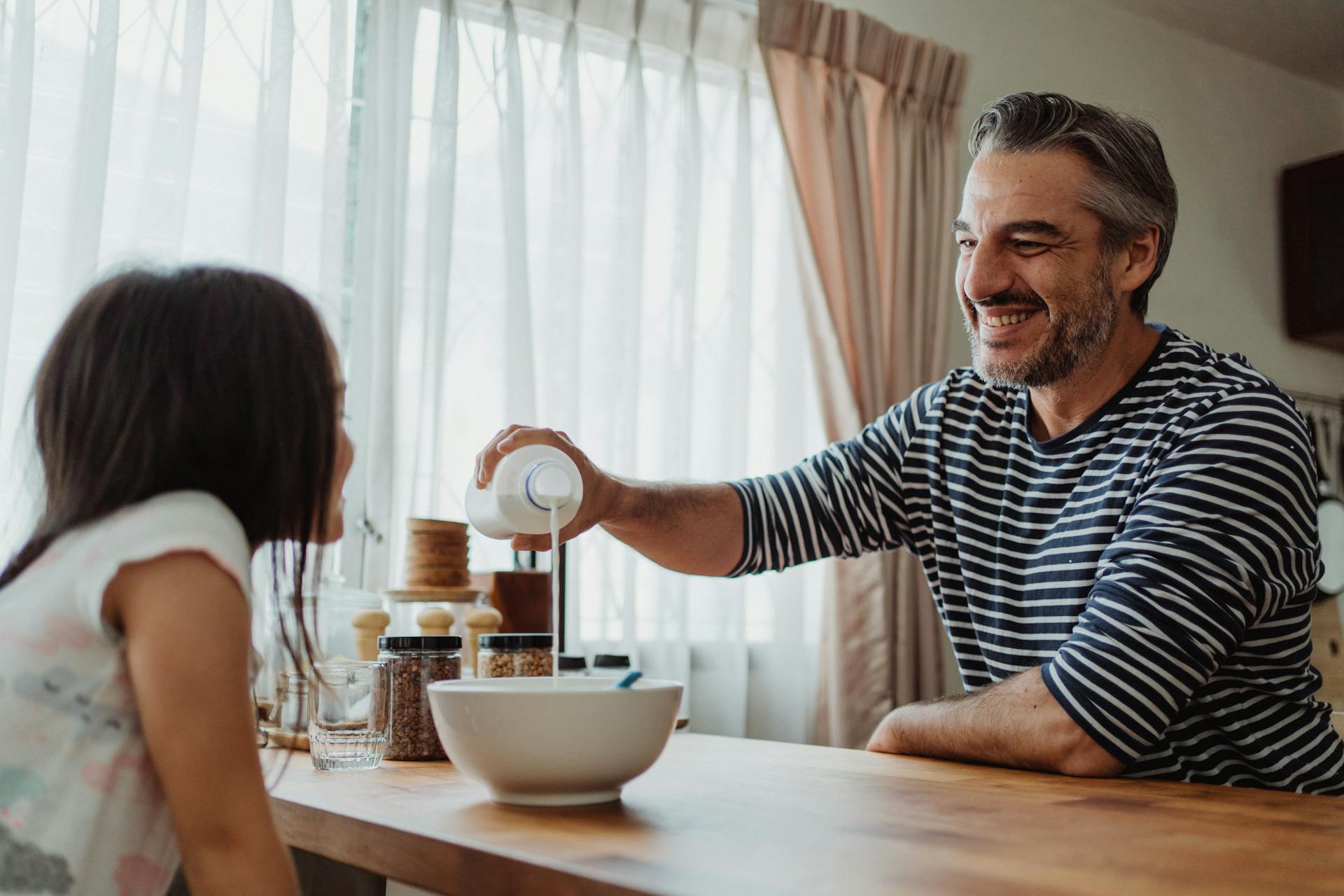A man pouring milk in a bowl while his daughter watches him | Source: Pexels