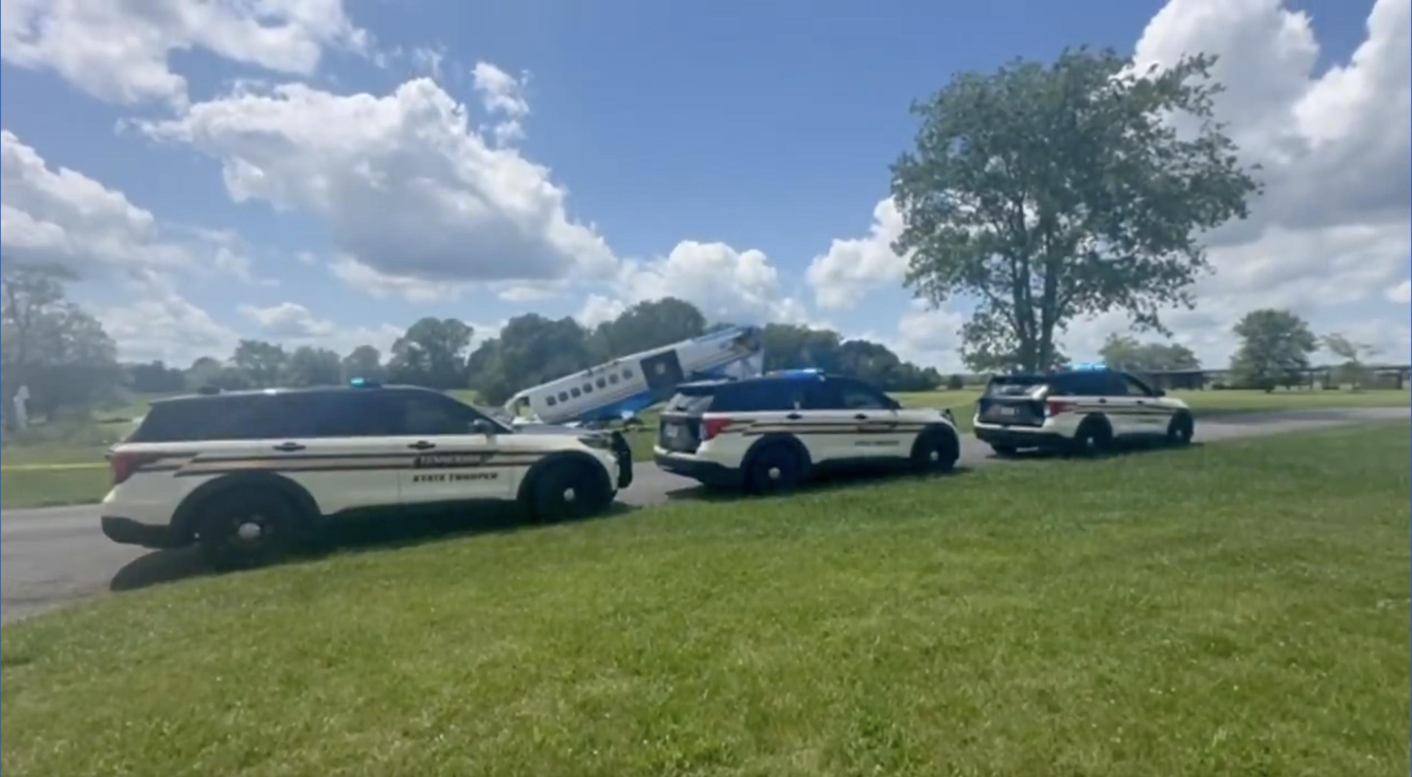 Three Tennessee State Trooper SUVs are seen parked near the crash site, with the skydiving aircraft in the background tilted with its nose on the ground, on June 8, 2025 | Source: x/TNHighwayPatrol