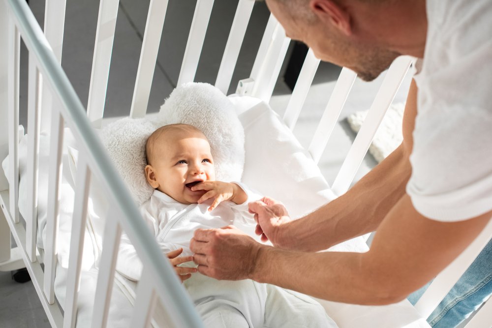 A photo of father watching his infant daughter in a baby crib. | Photo: Shutterstock