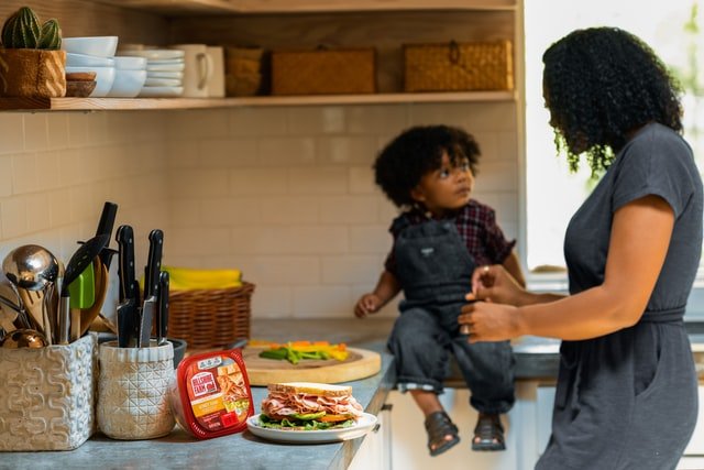 Un garçon assis sur le comptoir de la cuisine pendant que sa mère prépare à manger | Source : Unsplash