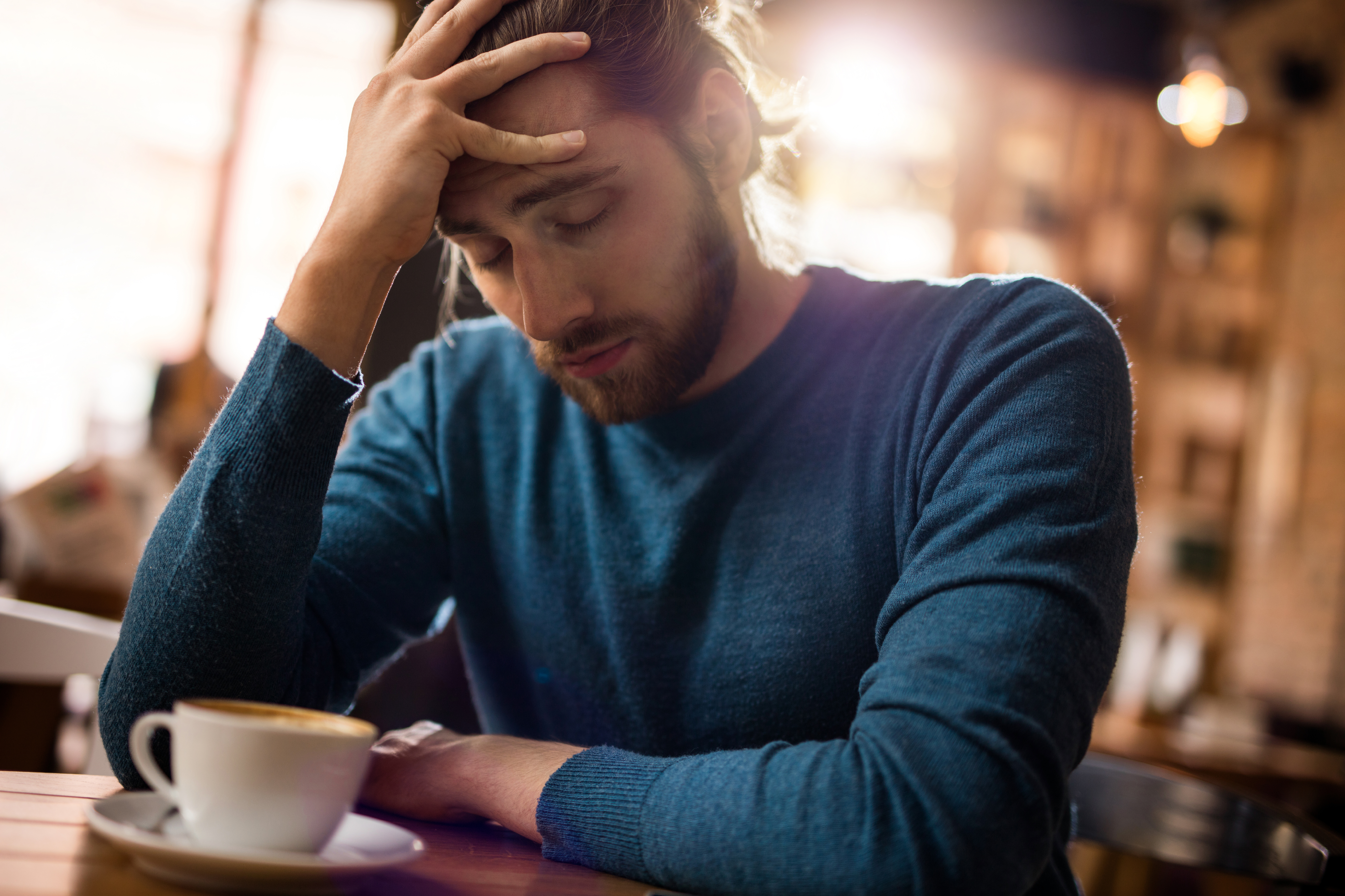Stressed man holding his head in pain in a cafe | Source: Getty Images