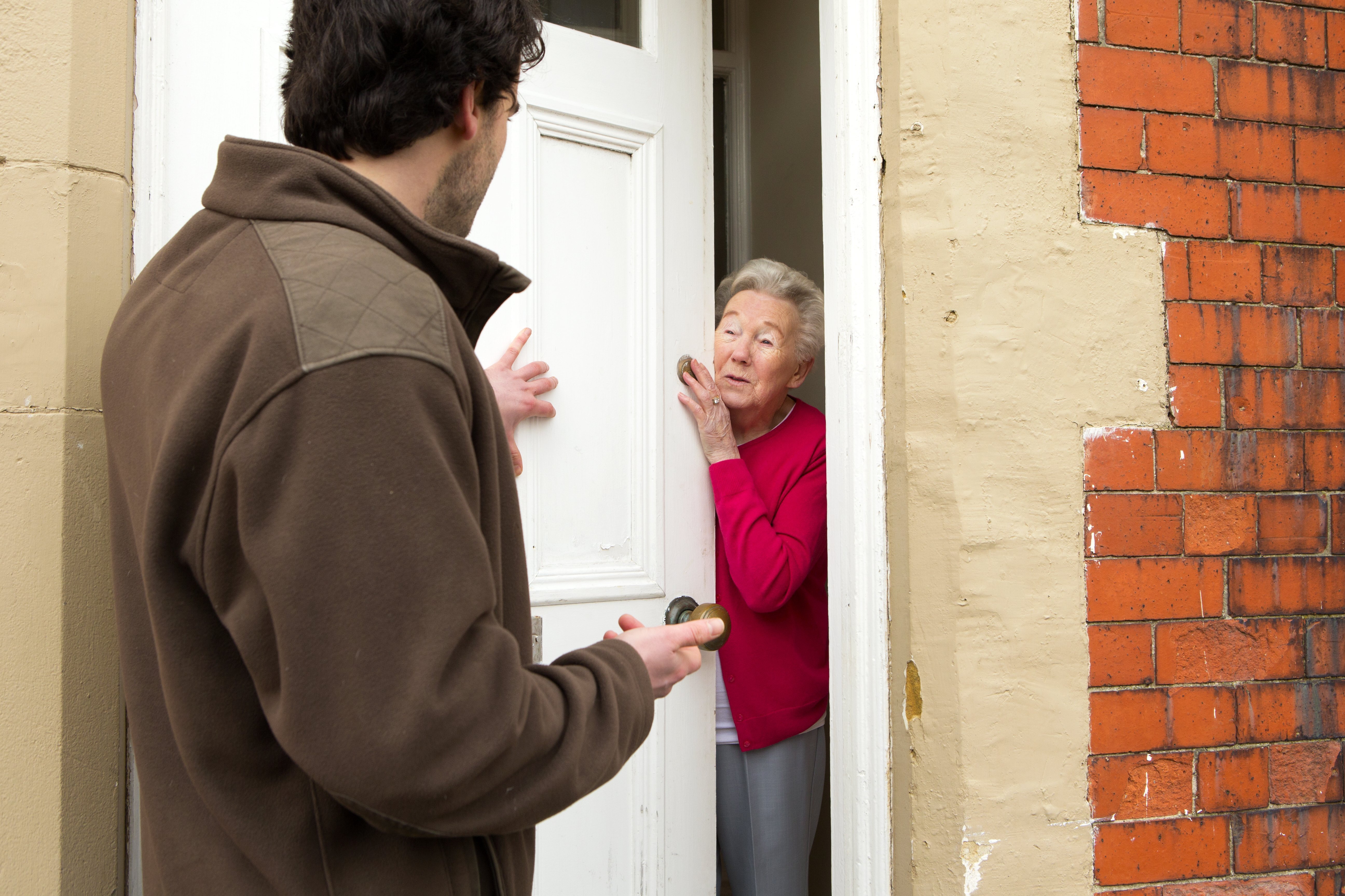 A horizontal image of a male door salesman putting an older lady under pressure to buy. | Photo: Getty Images