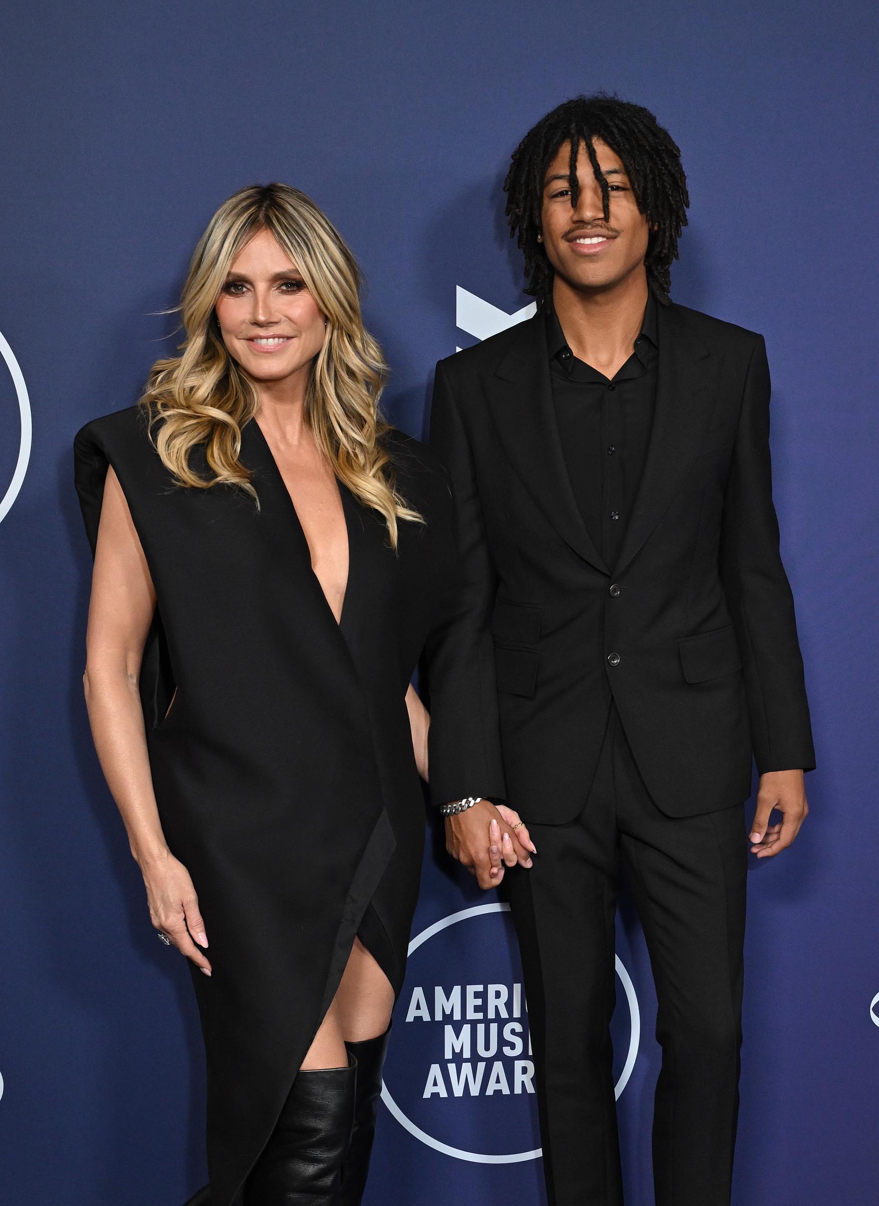 Henry Samuel offers a subtle smile while standing hand-in-hand with Heidi Klum. His reserved expression and steady posture add a poised note to the duo’s coordinated red carpet appearance.