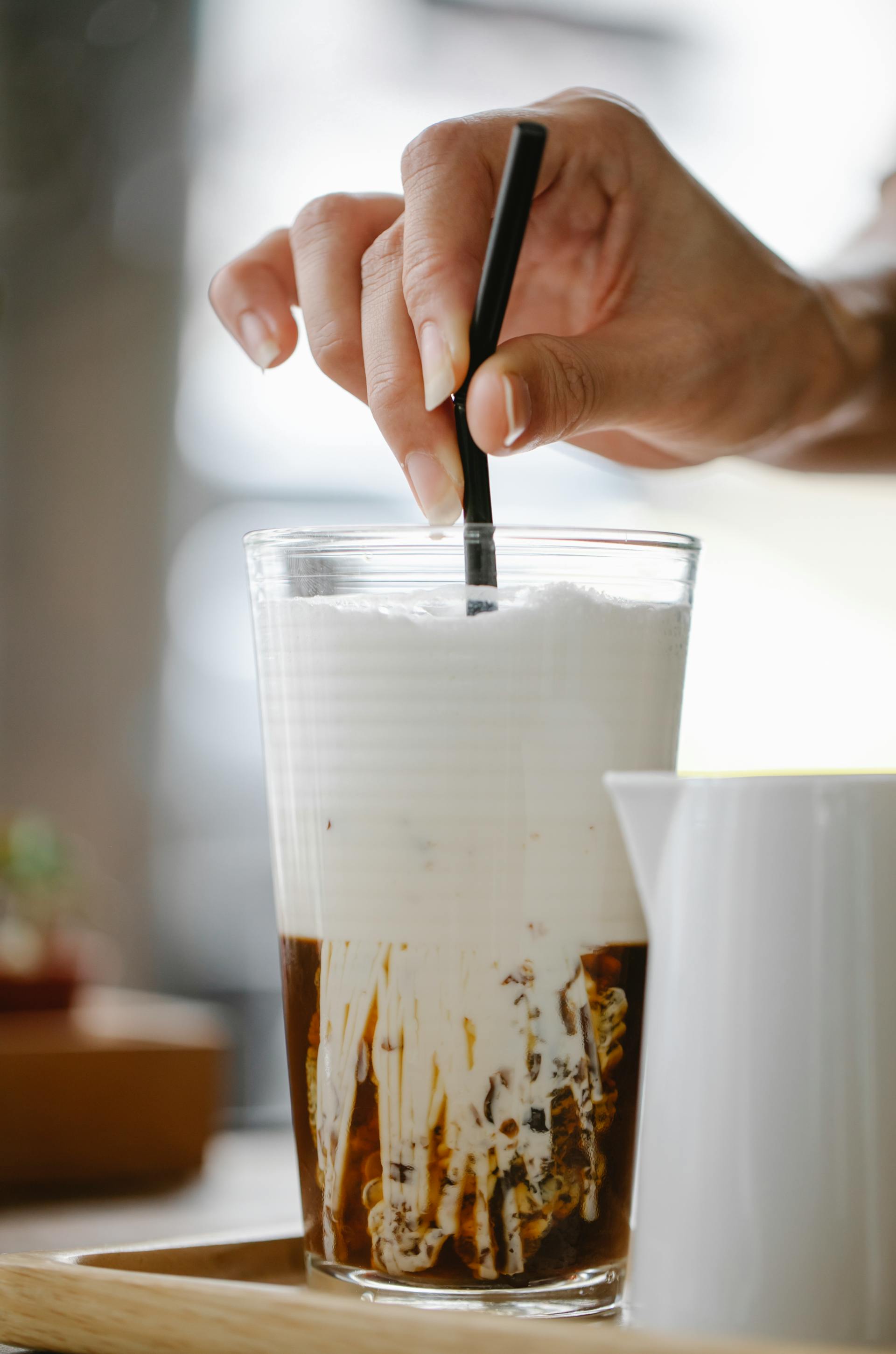 A closeup shot of a woman stirring her iced coffee with a straw | Source: Pexels