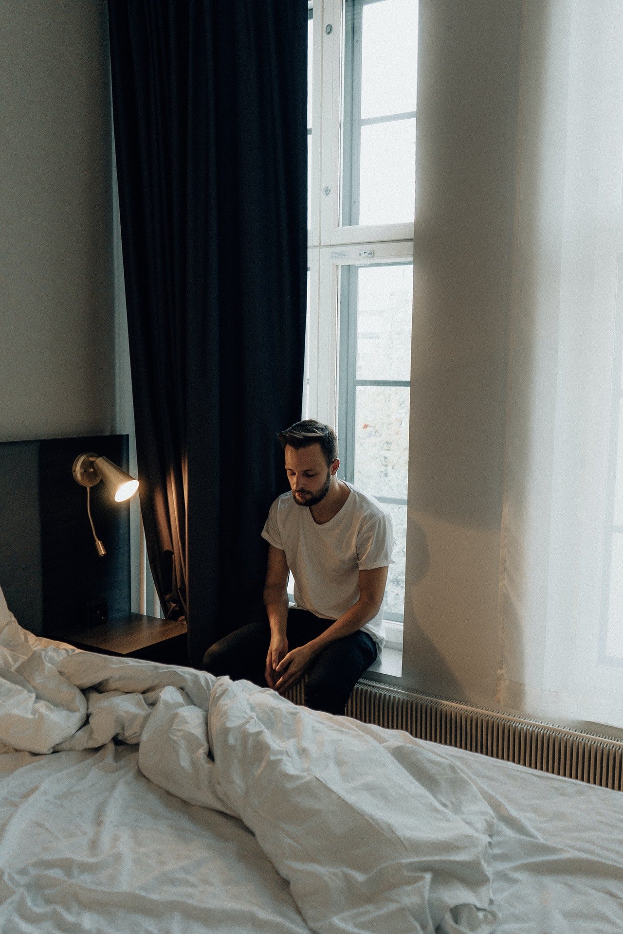 Un hombre joven reflexiona frente a su cama. | Foto: Pexels