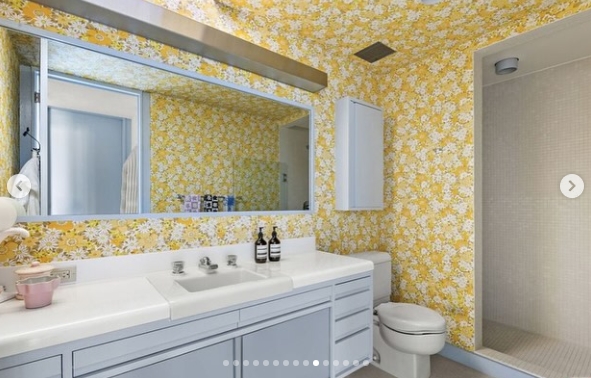 One bathroom takes a dramatically different approach, with yellow-and-white floral wallpaper covering the walls and giving the space a playful retro character. The bold print contrasts with pale blue cabinetry, a white countertop, and a simple tiled shower, creating one of the home's most distinctive decorative moments. | Source: Instagram/jparkerstanton