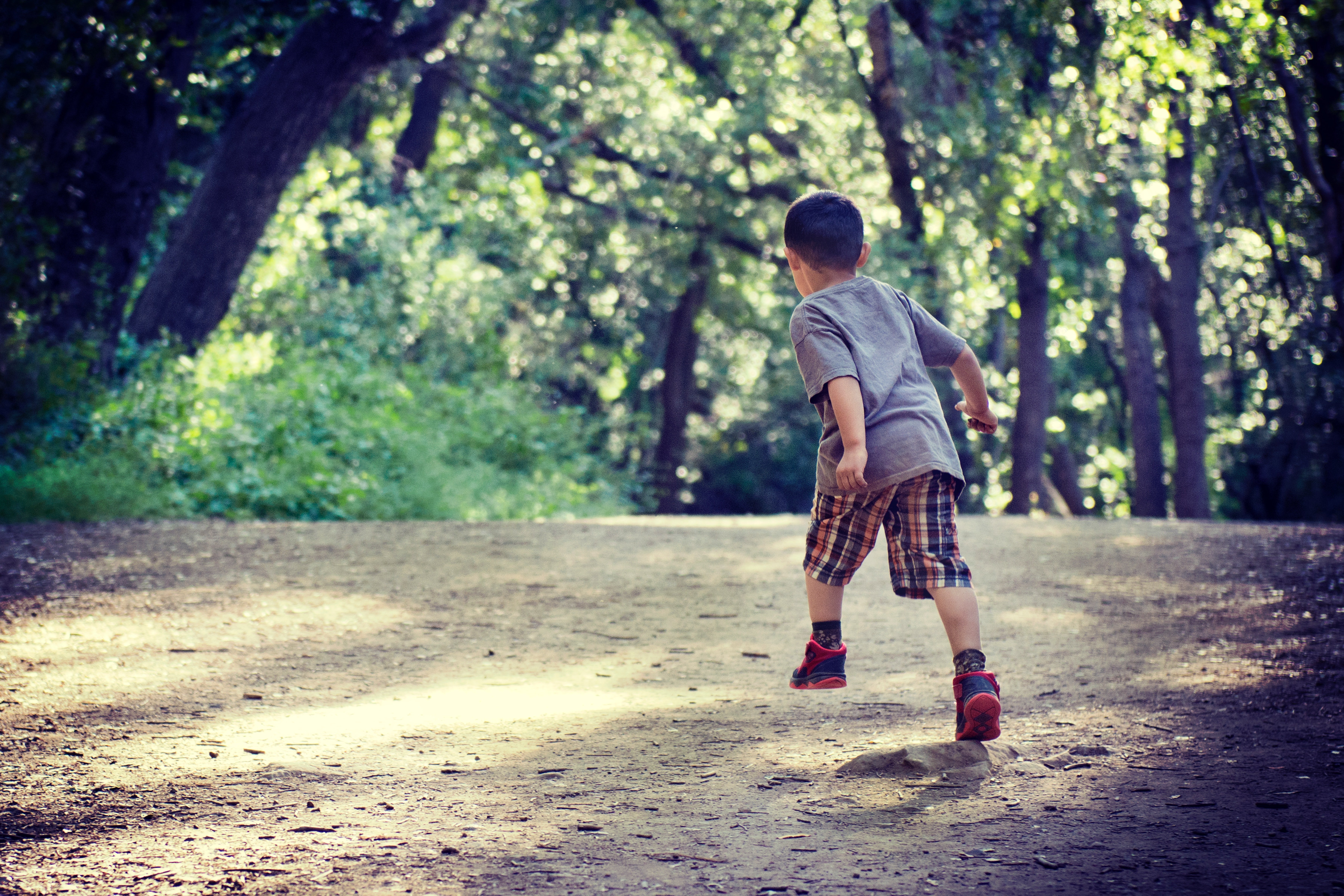 Niño corriendo a través de un camino de tierra rodeado de árboles. | Foto: Unsplash