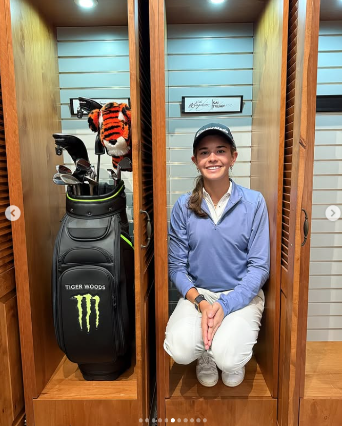 Kai sits and smiles inside a wooden locker next to Tiger Woods' golf bag | Source: Facebook/Kai-Trump