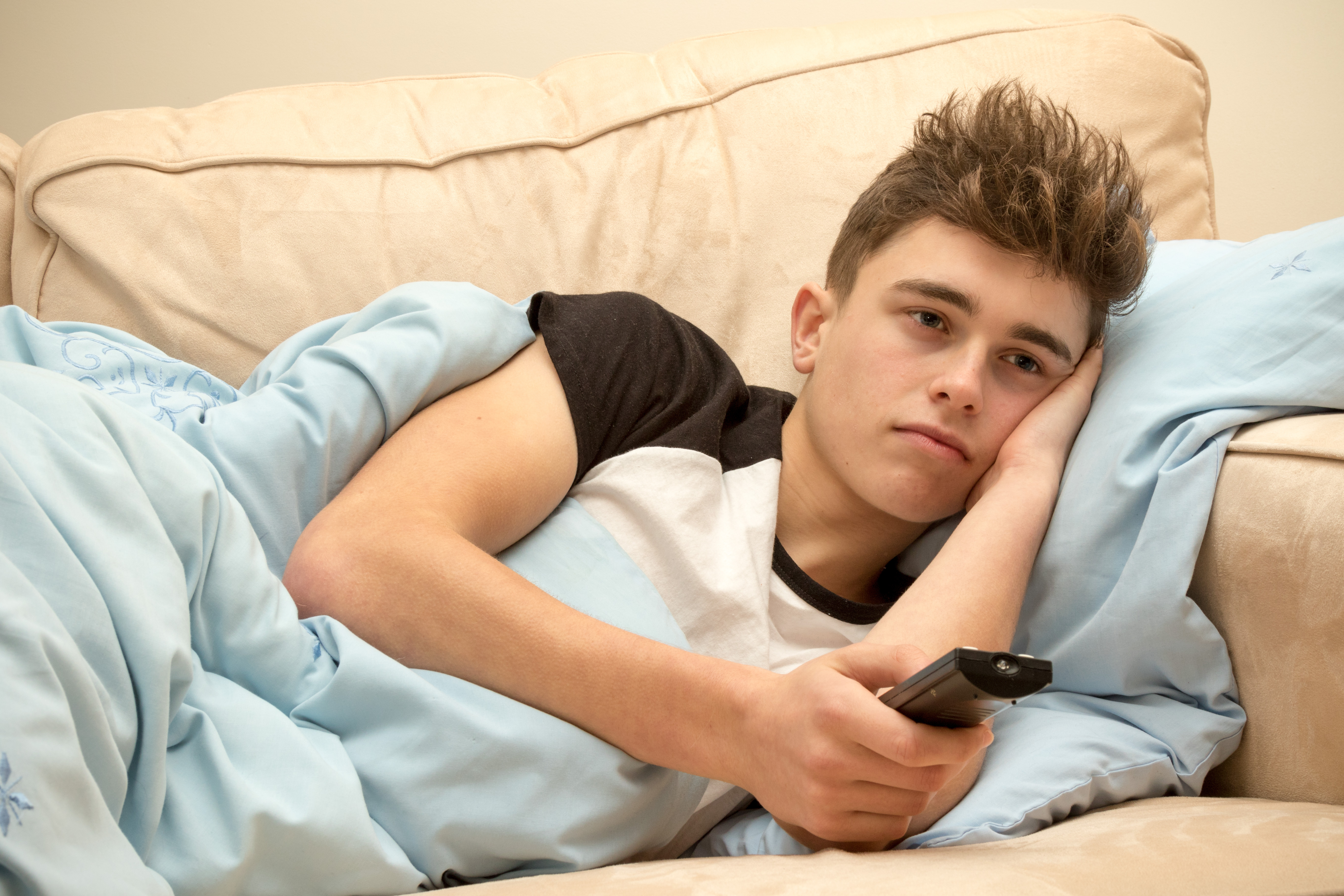 A lazy young man watching TV on a sofa | Source: Shutterstock