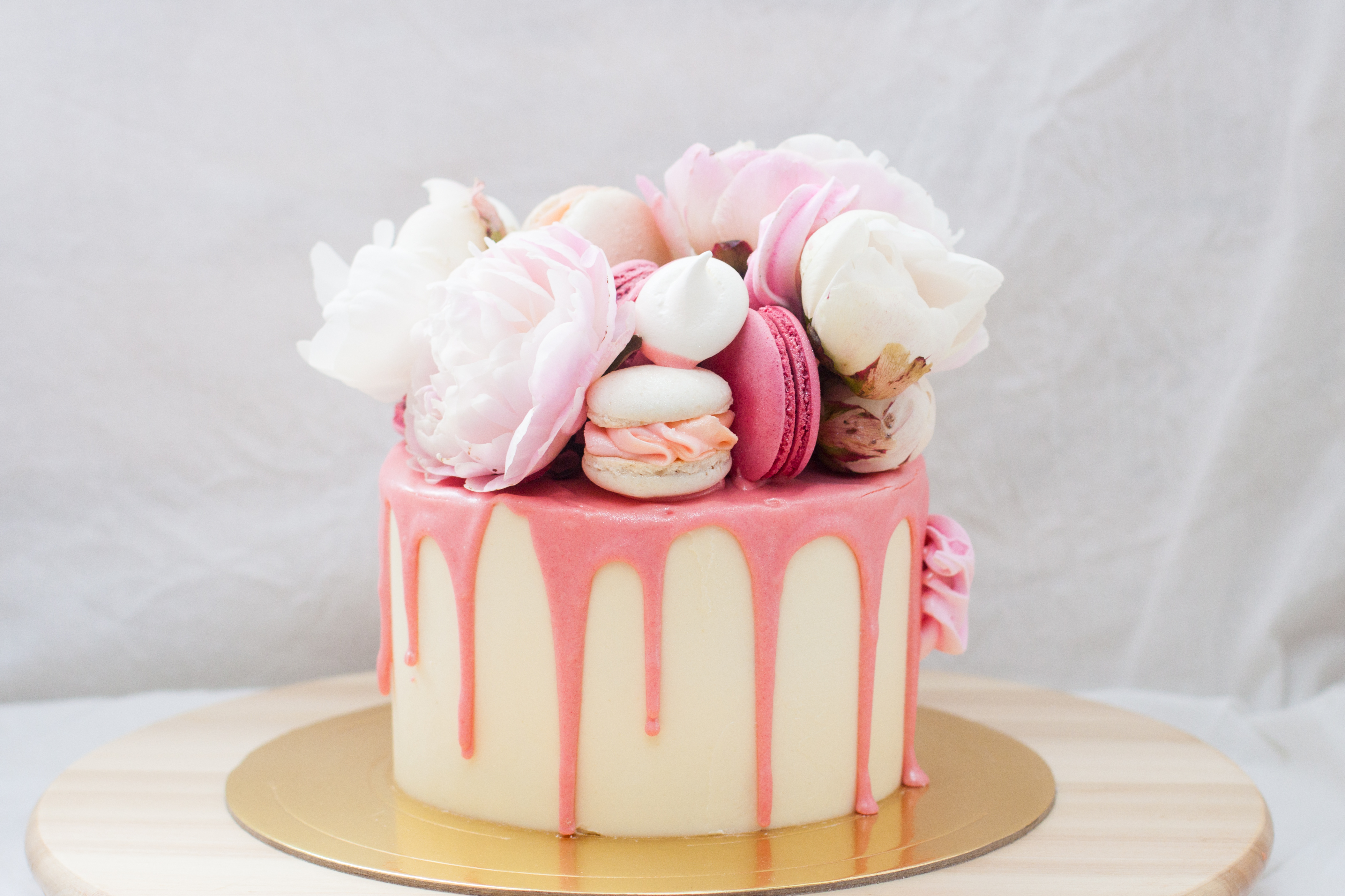 Small birthday cake with melted pink chocolate, fresh peonies, macaroons and meringues on white background | Source: Getty Images