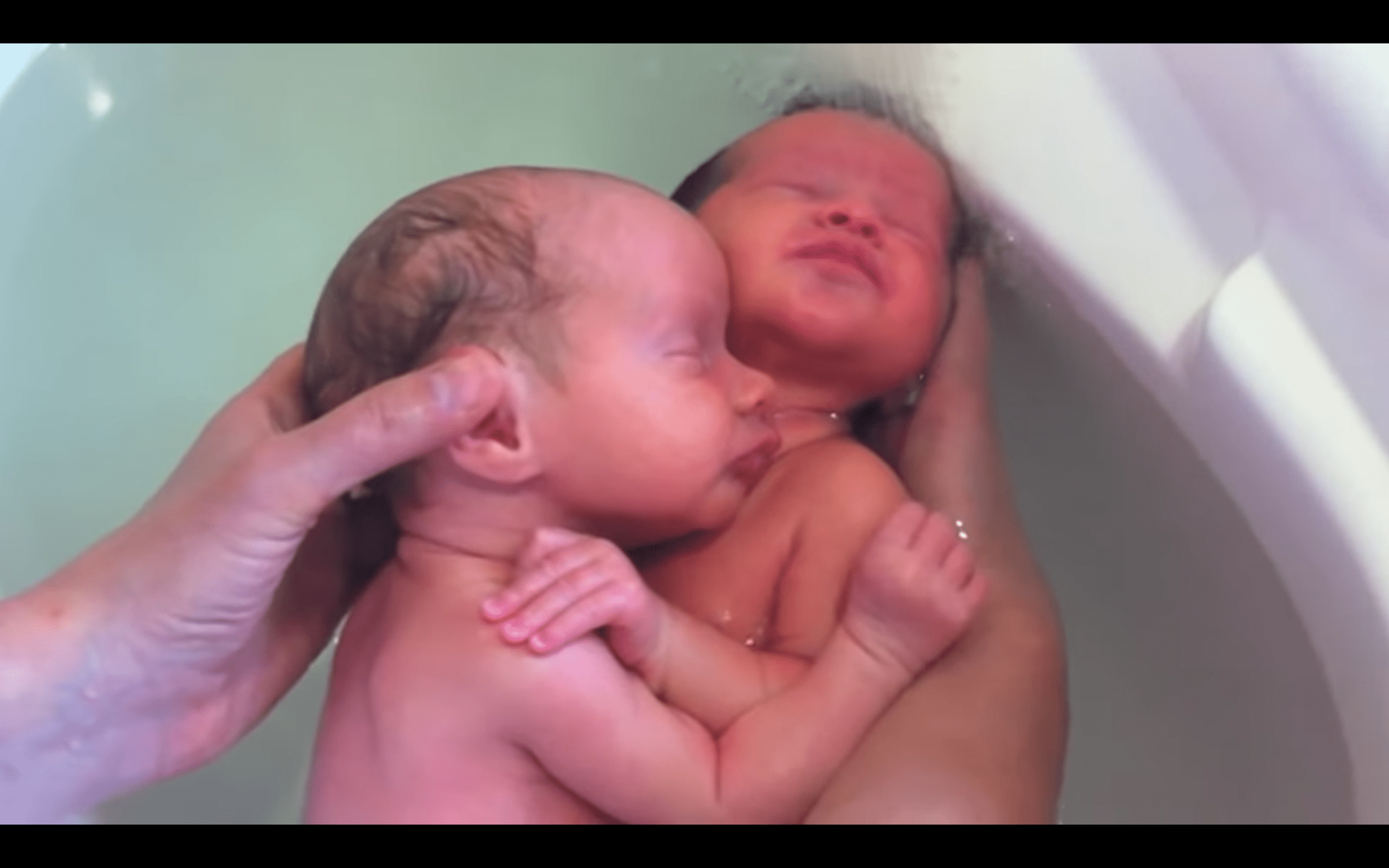 Twin babies holding on to each other in a video shared by a nurse bathing them. | Photo: youtube.com/massagebebe