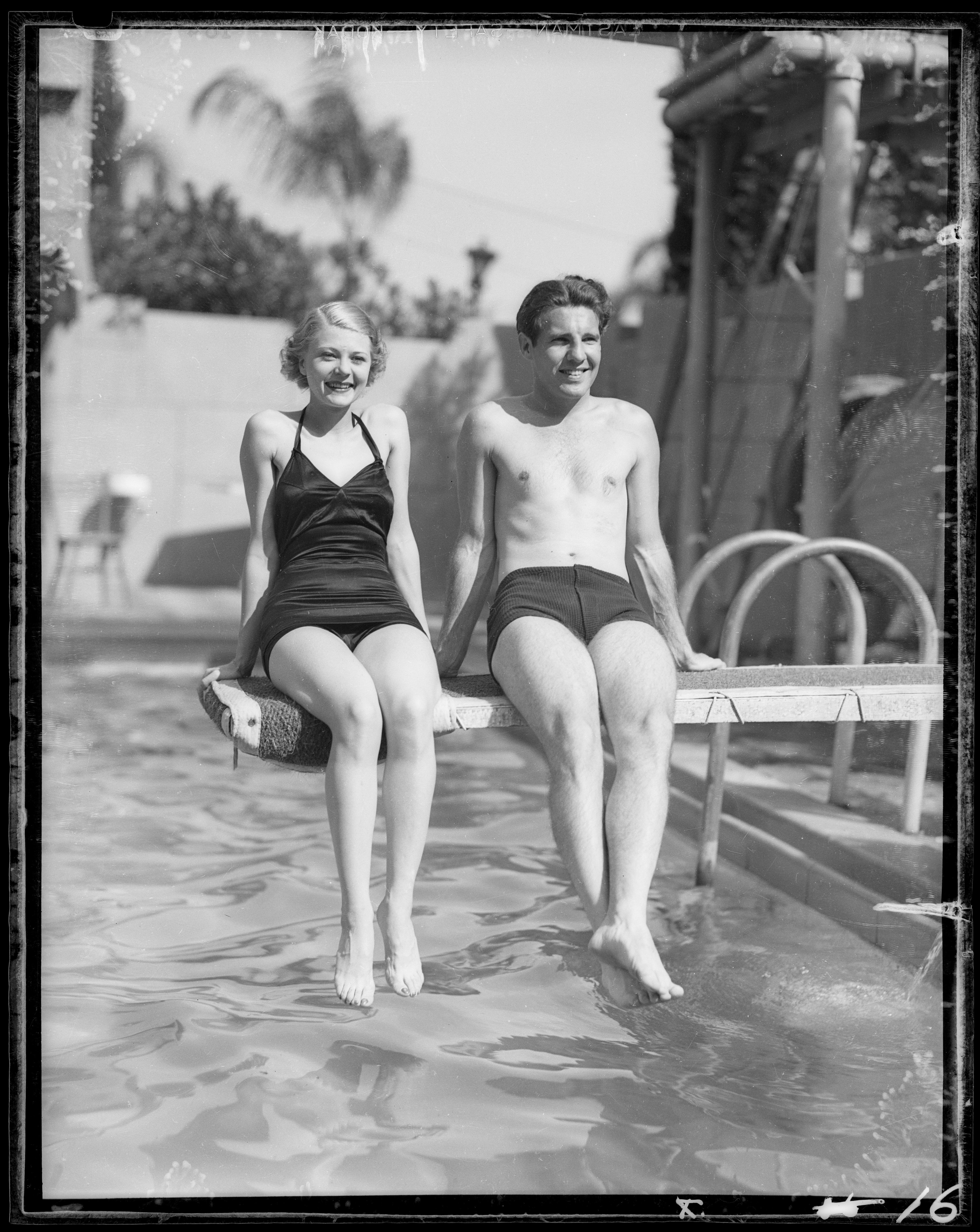 Harriet Hilliard and Ozzie Nelson in bathing suits sitting on a diving board above a pool at The Ambassador Hotel in Los Angeles, California, circa 1935. | Source: Dick Whittington Studio/Corbis/Getty Images